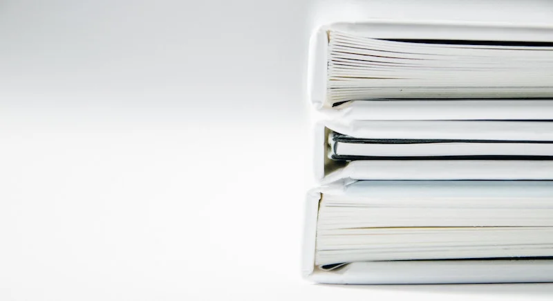 Stack of white binders filled with paper documents.