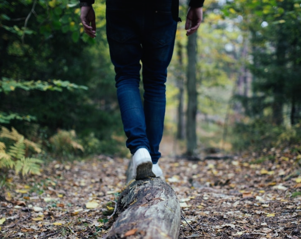 A person balancing on a log while walking through the forest.