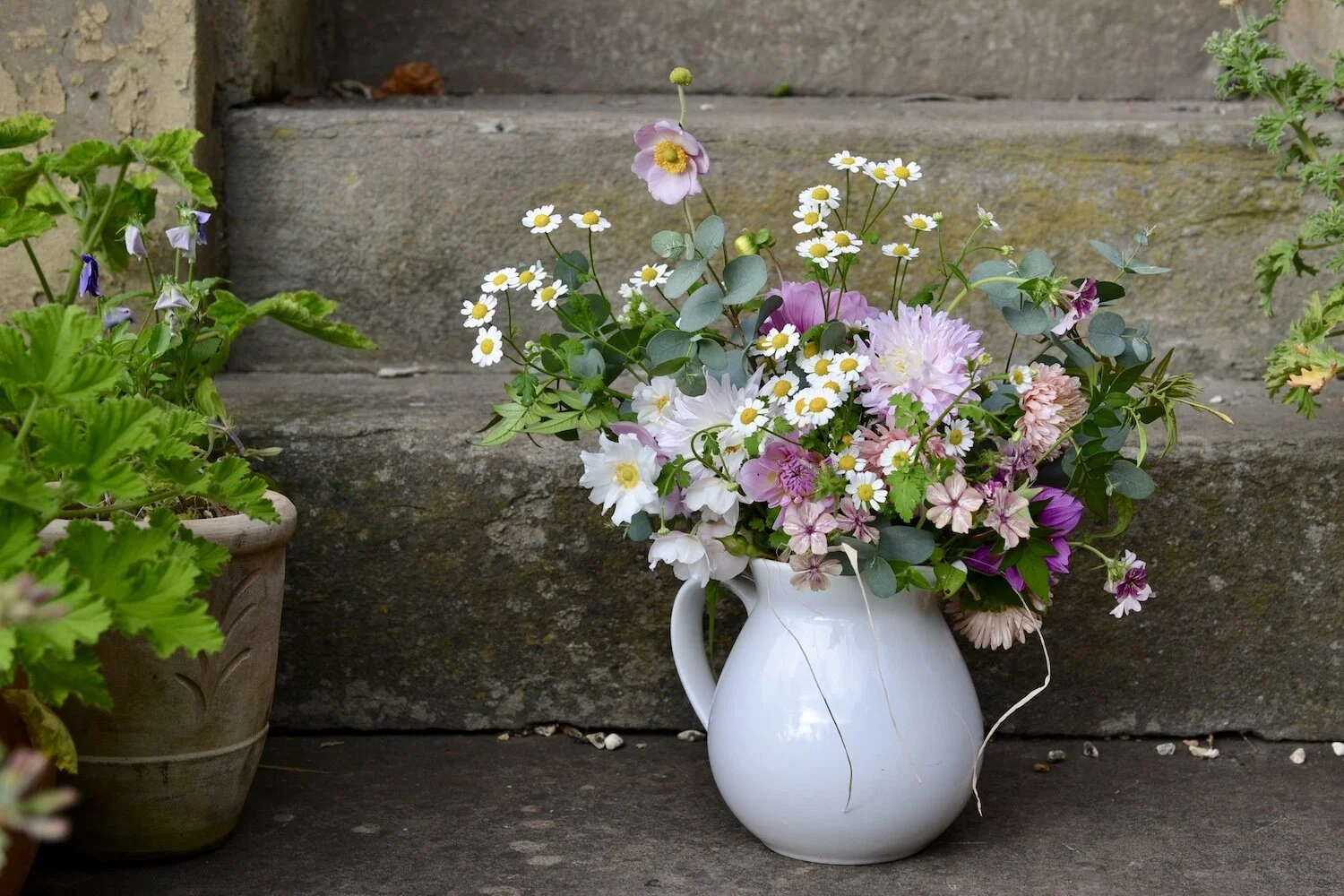 Pink and white flowers in a white jug sitting on stone steps