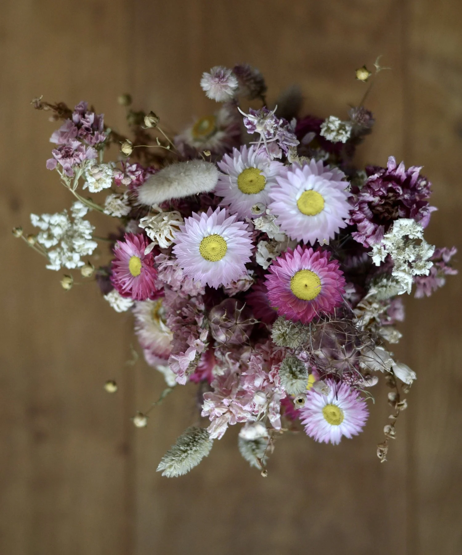 Dried bouquet of pink flowers standing on wooden table, viewed from above.