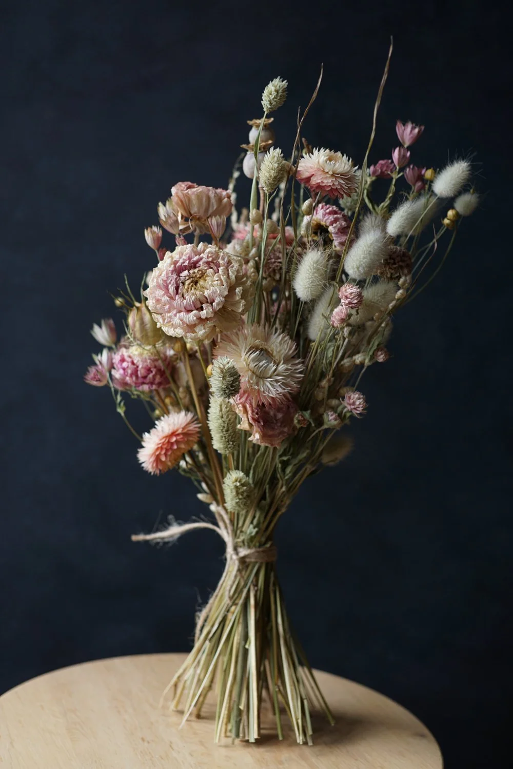 Bouquet of dried pink flowers, standing on a wooden tabletop against a black background.