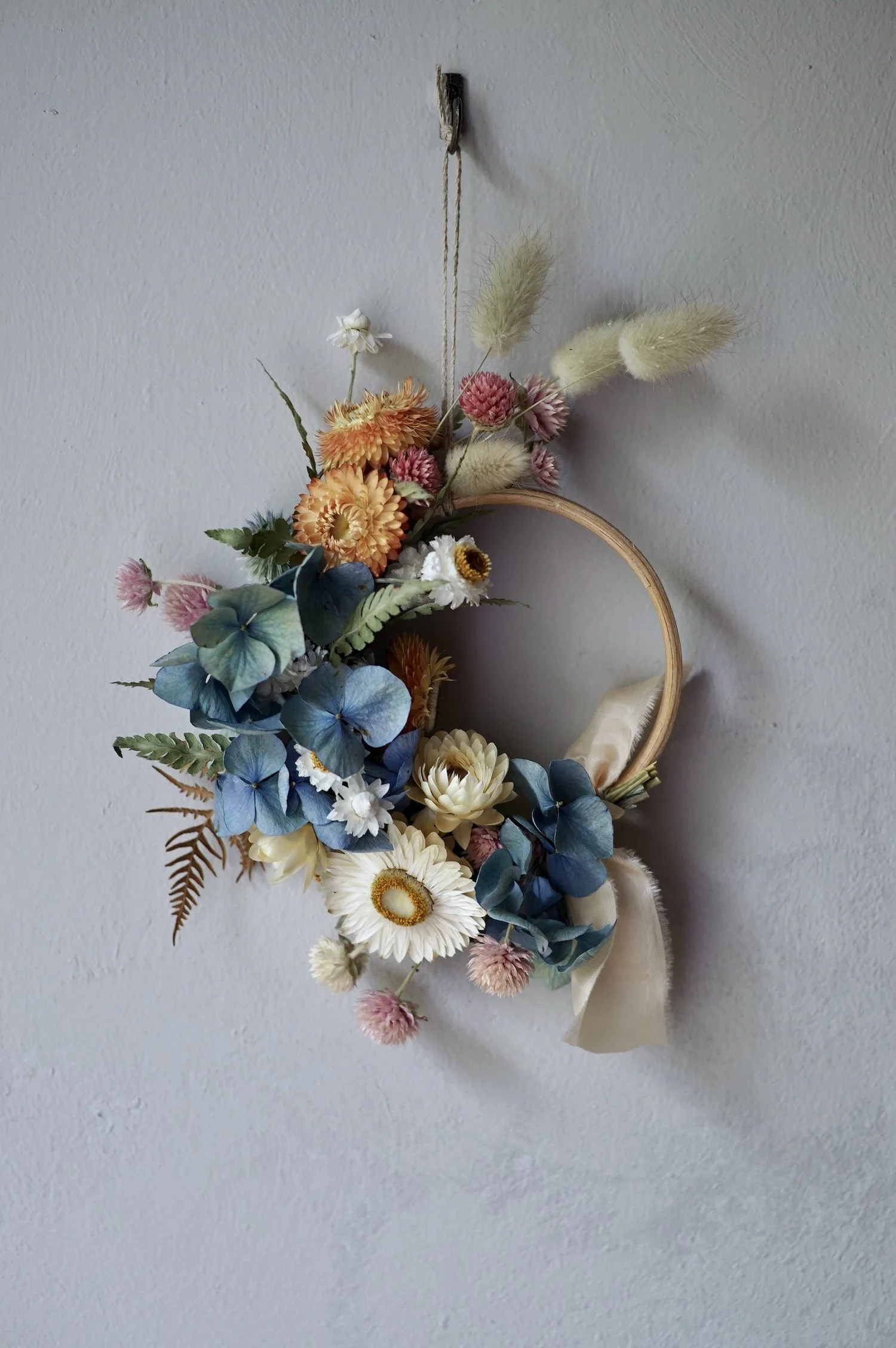 Mini dried flower wreath of pastel coloured flowers and a pale peach ribbon.