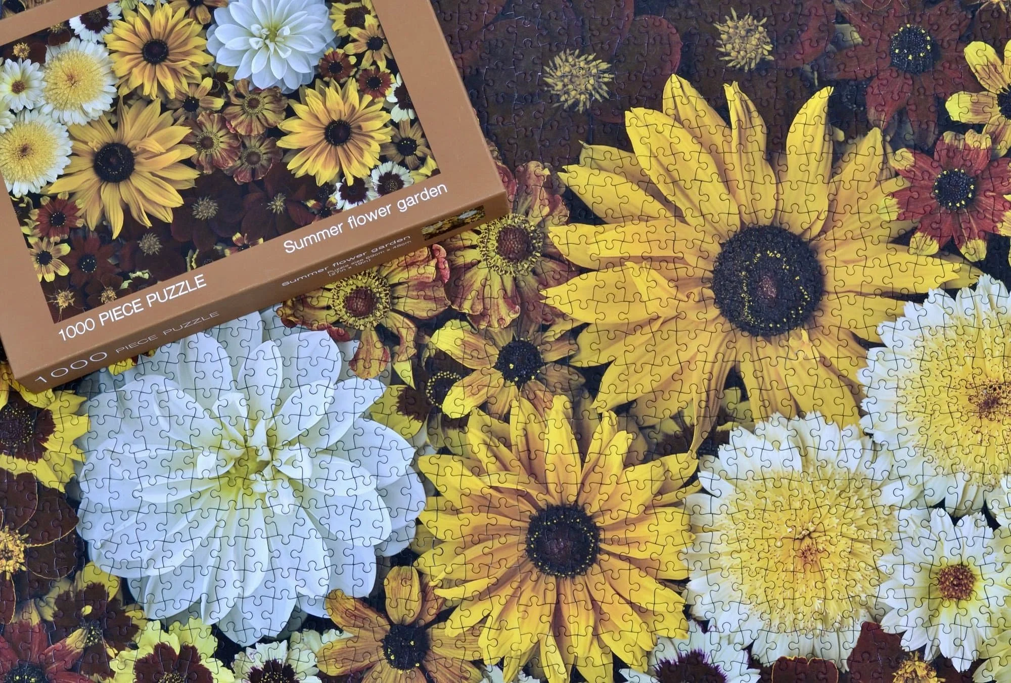 A picture of an assembled summer flowers jigsaw puzzle with the box top showing the picture sitting on top.