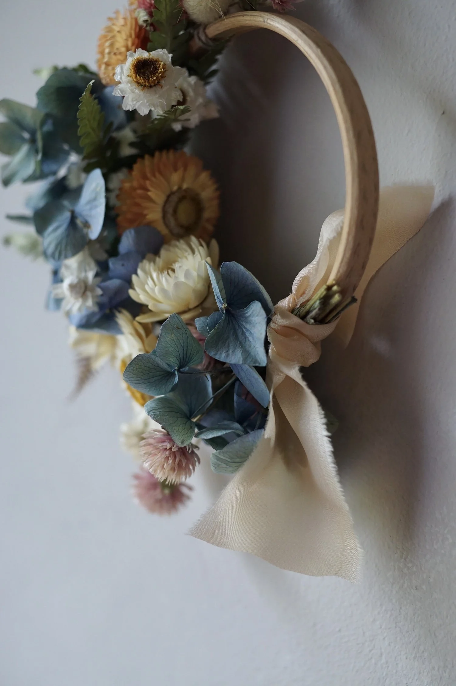 Mini dried flower wreath of pastel coloured flowers and a pale peach ribbon.