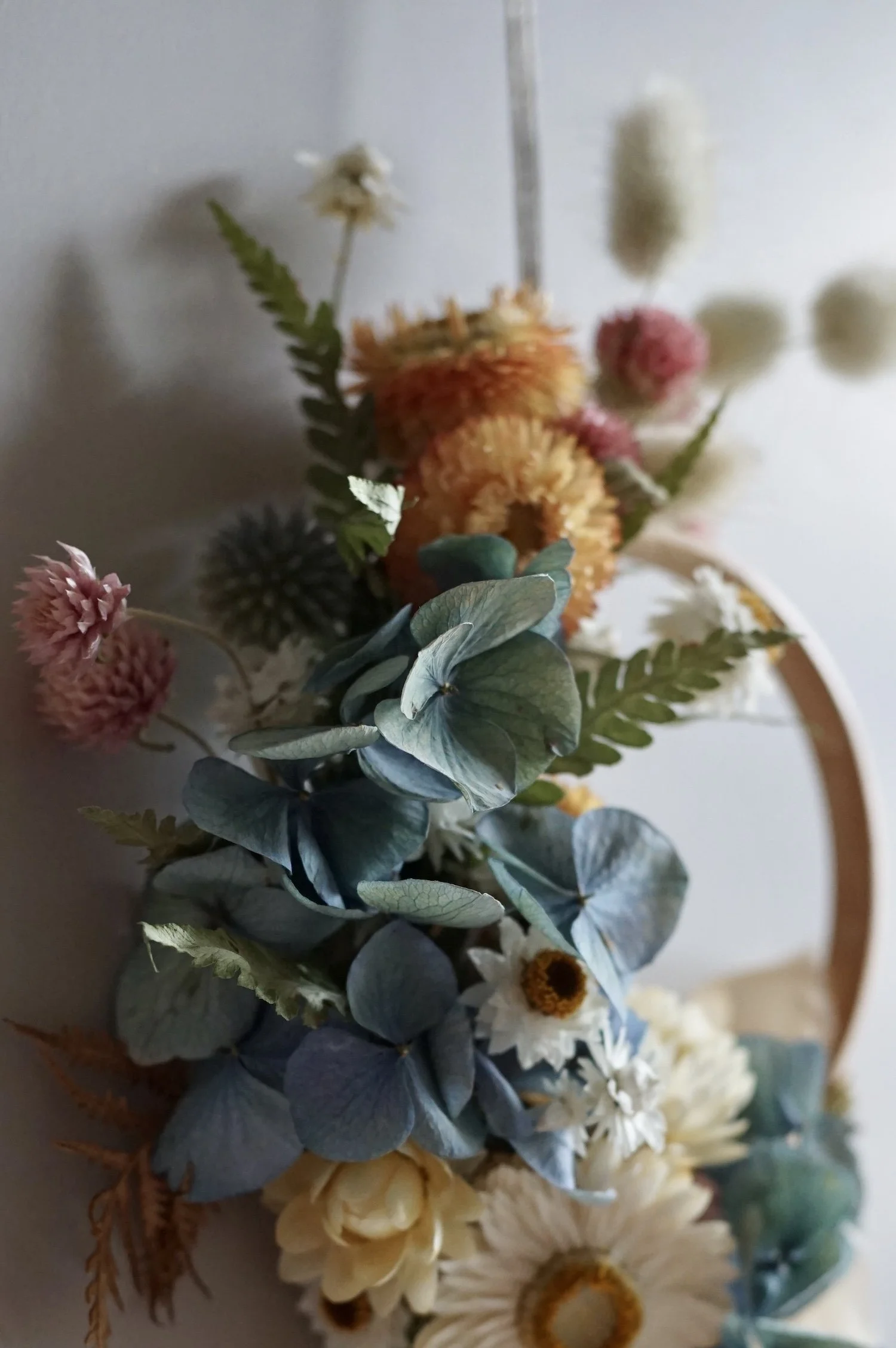 Mini dried flower wreath of pastel coloured flowers and a pale peach ribbon.