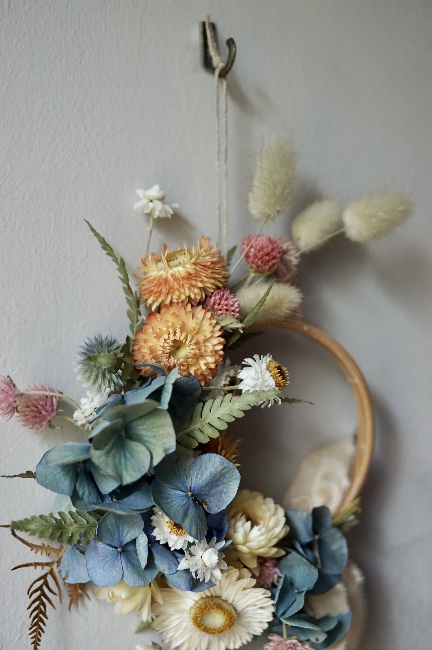 Mini dried flower wreath of pastel coloured flowers and a pale peach ribbon.