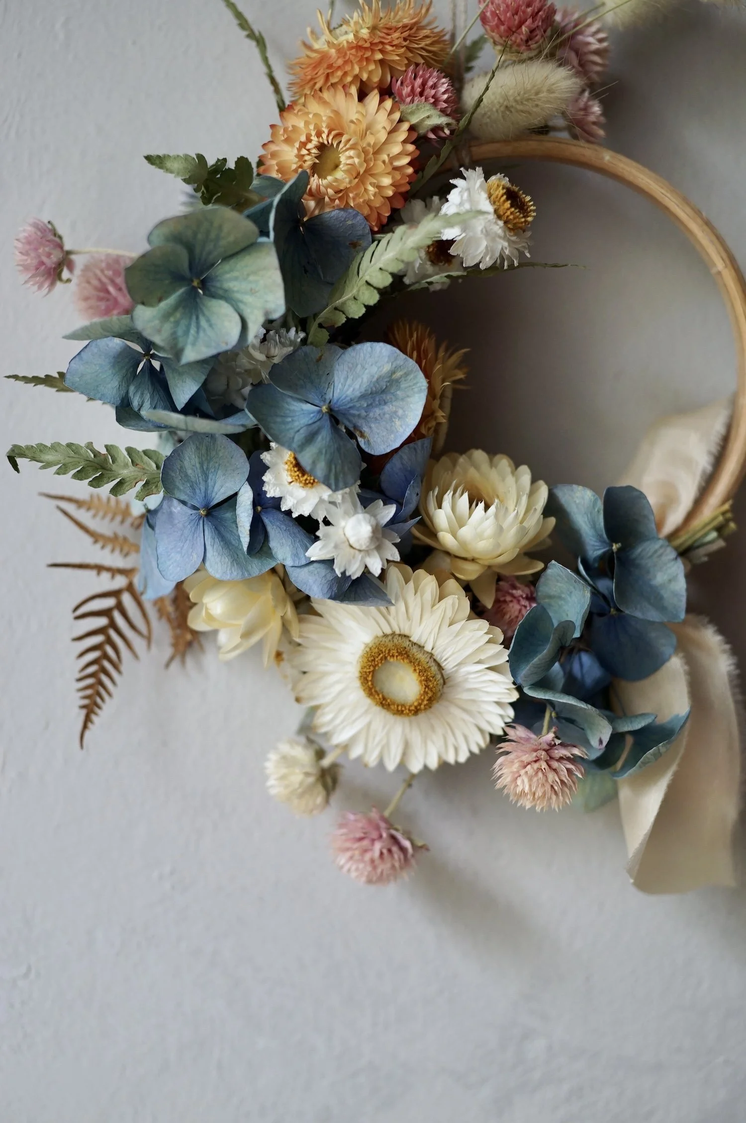 Mini dried flower wreath of pastel coloured flowers and a pale peach ribbon.