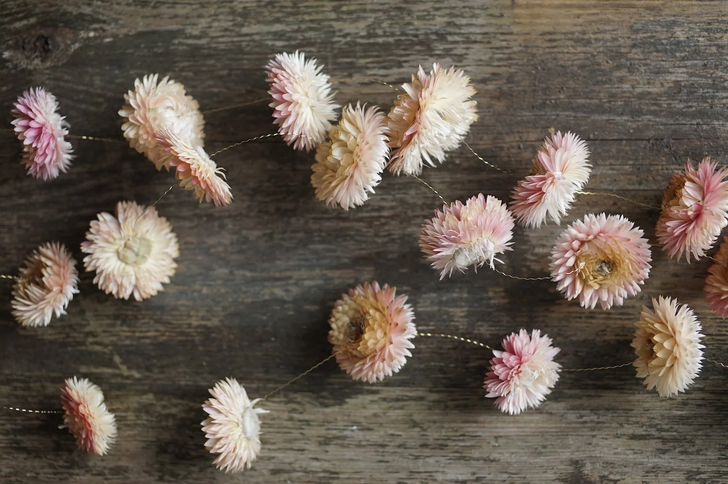 Several flower garlands made from pale pink dried flowers and gold wire laying on a piece of wood