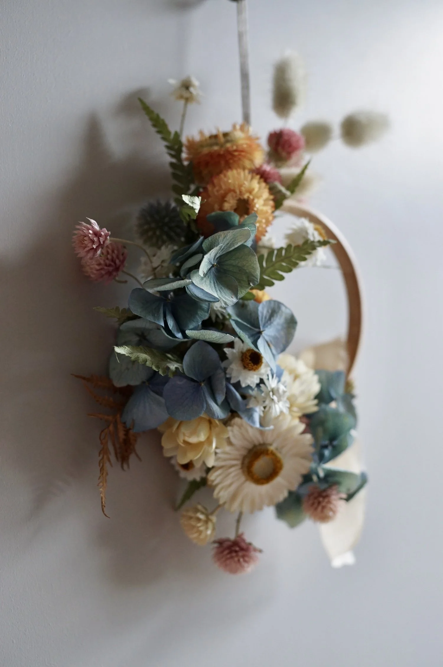 Mini dried flower wreath of pastel coloured flowers and a pale peach ribbon.