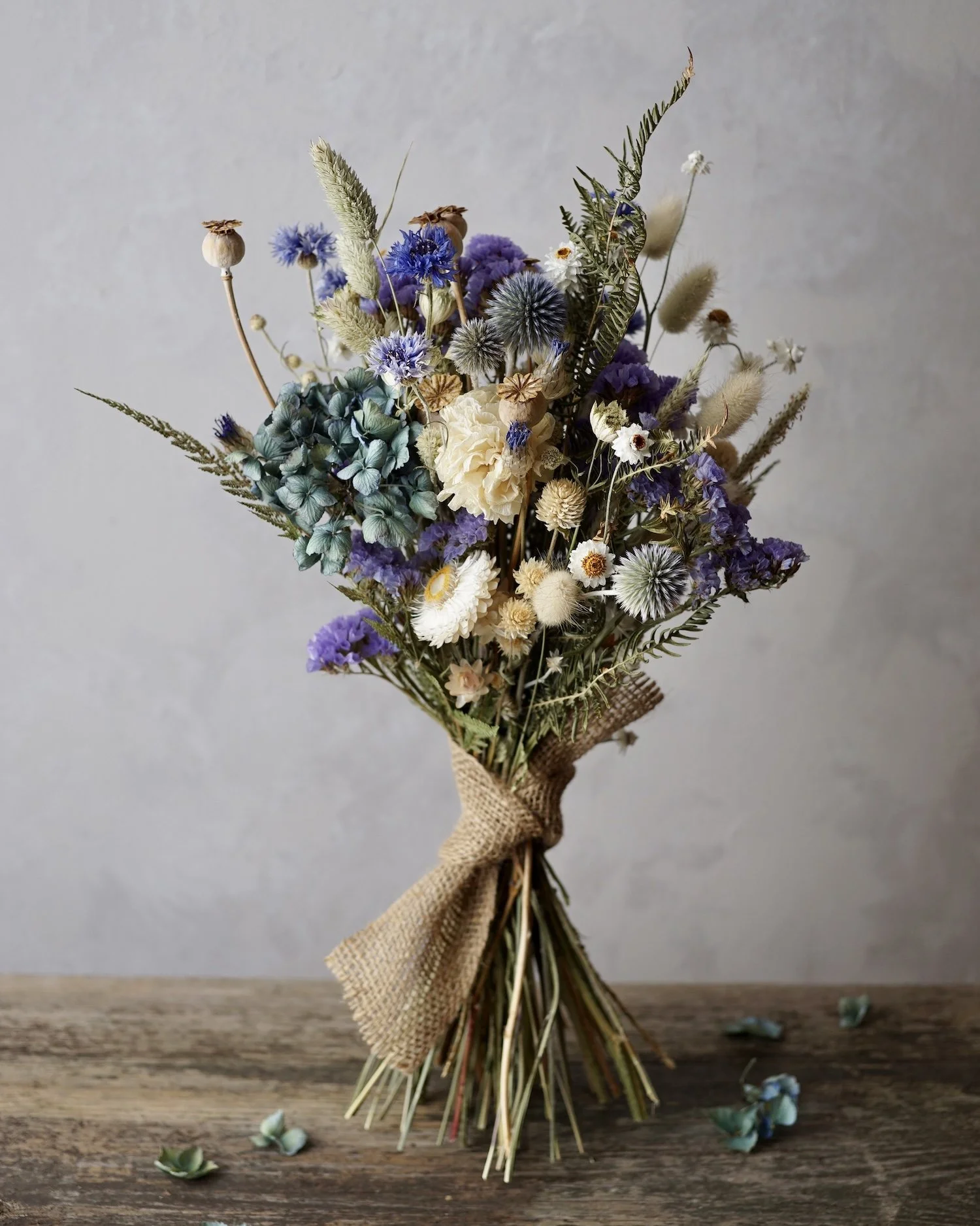 A blue themed dried flower bouquet standing on a wooden table