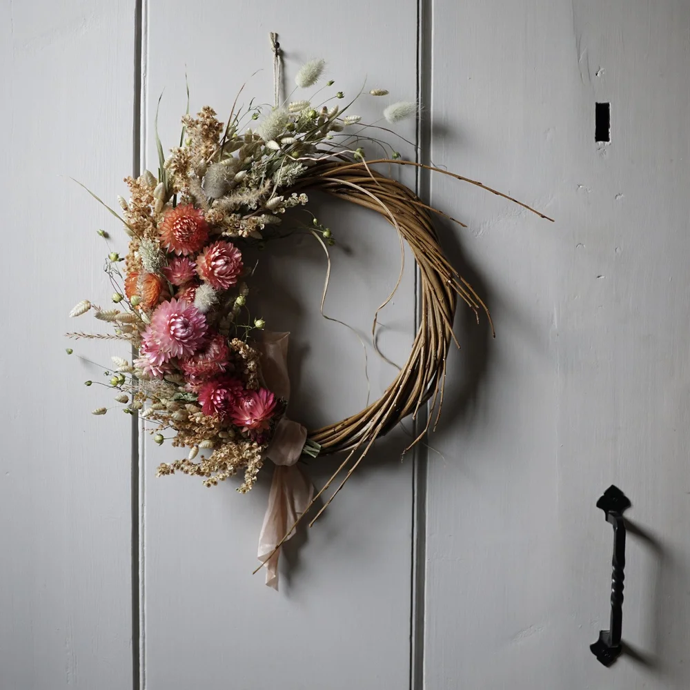 A dried flower wreath made from deep pink and orange strawflowers