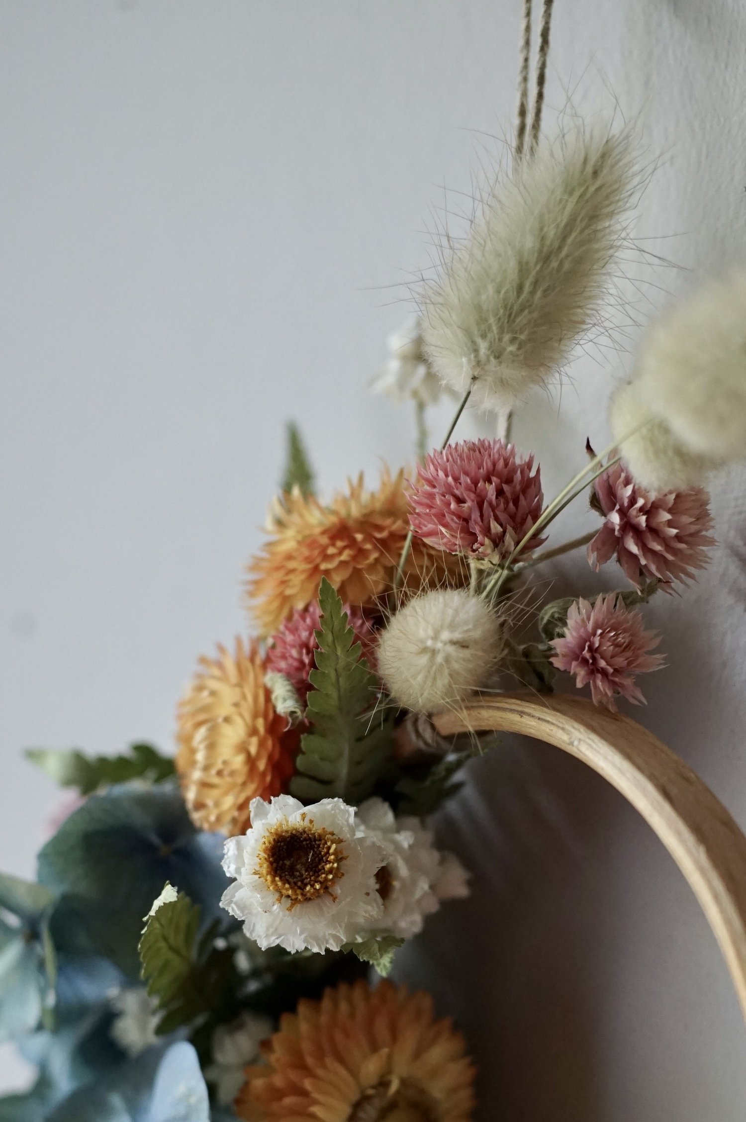 Close up photo of green fuzzy grass heads and orange flowers in a mini dried flower wreath.