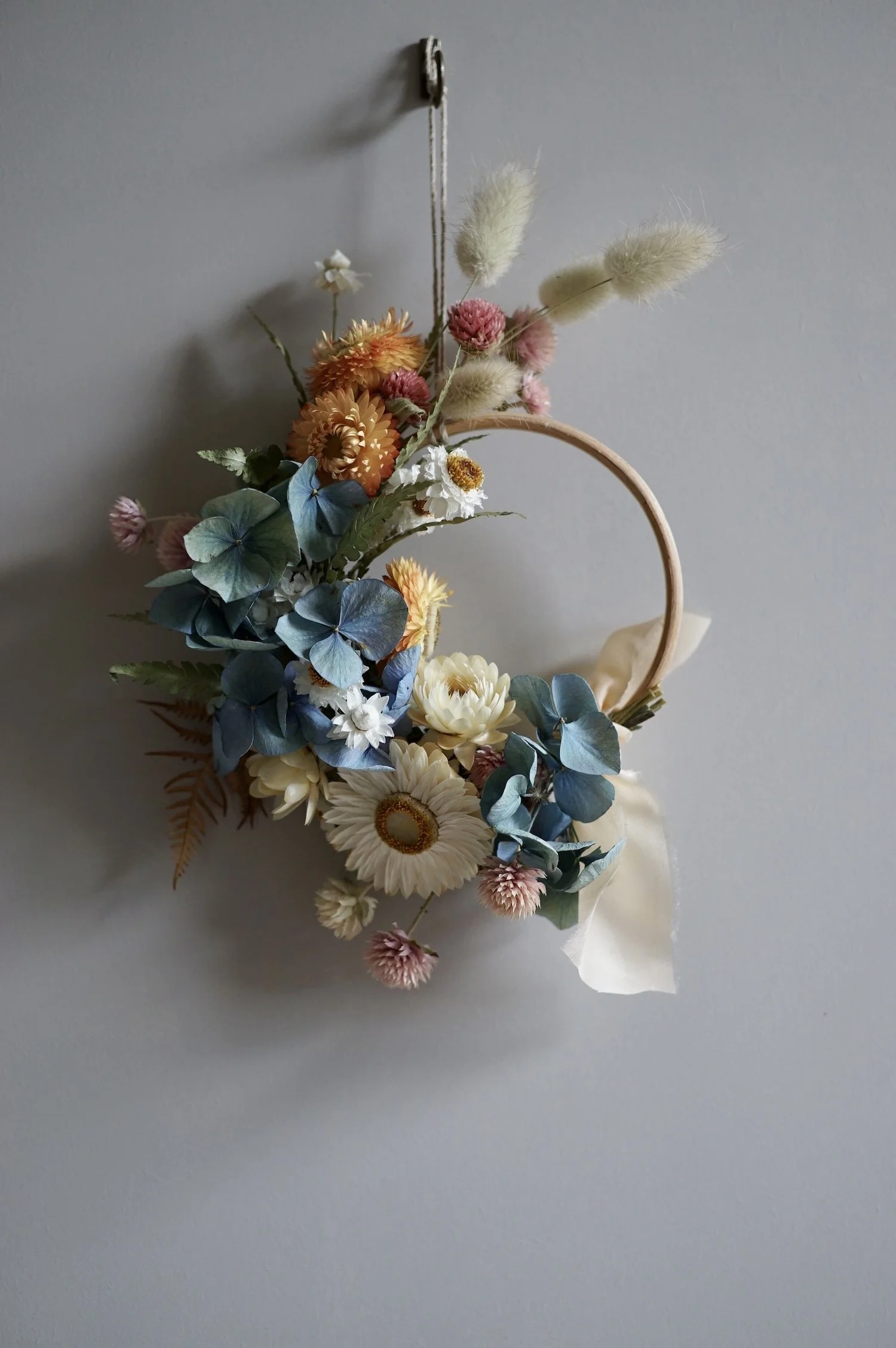 Mini dried flower wreath of pastel coloured flowers and a pale peach ribbon.
