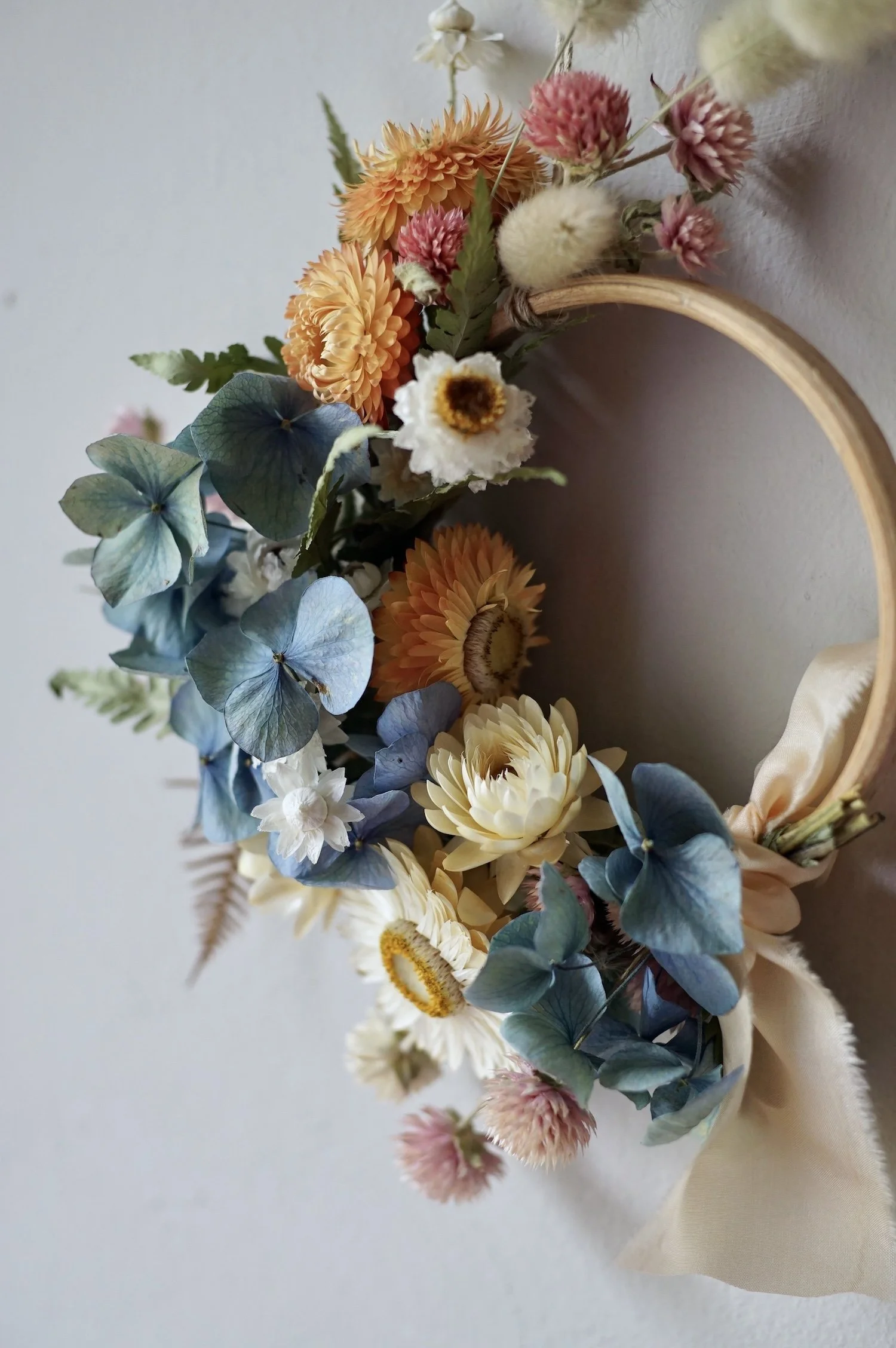 Mini dried flower wreath of pastel coloured flowers and a pale peach ribbon.