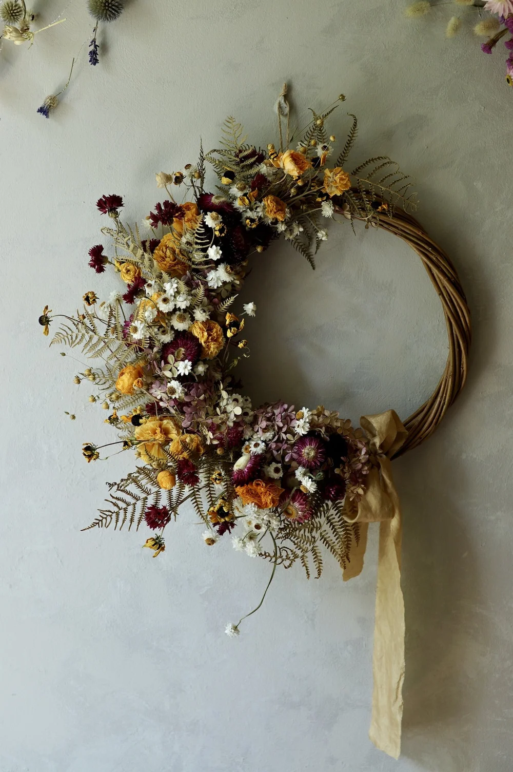 Dried flower wreath made with dried yellow ranunculus, dark red flowers and small white flowers
