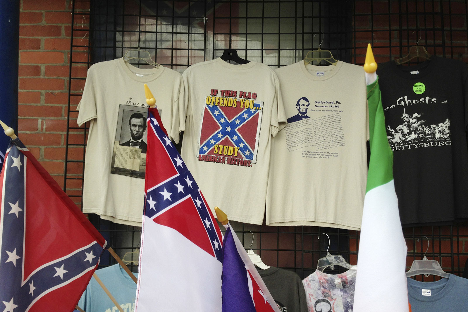 A tourist trap lures with overpriced t-shirts featuring US President Abraham Lincoln and his Gettysburg Address alongside multiple novelties featuring the Confederate flag and a shirt advertising The Ghosts of Gettysburg. The shirt in the middle reads, “If this flag offends you … study American history.”