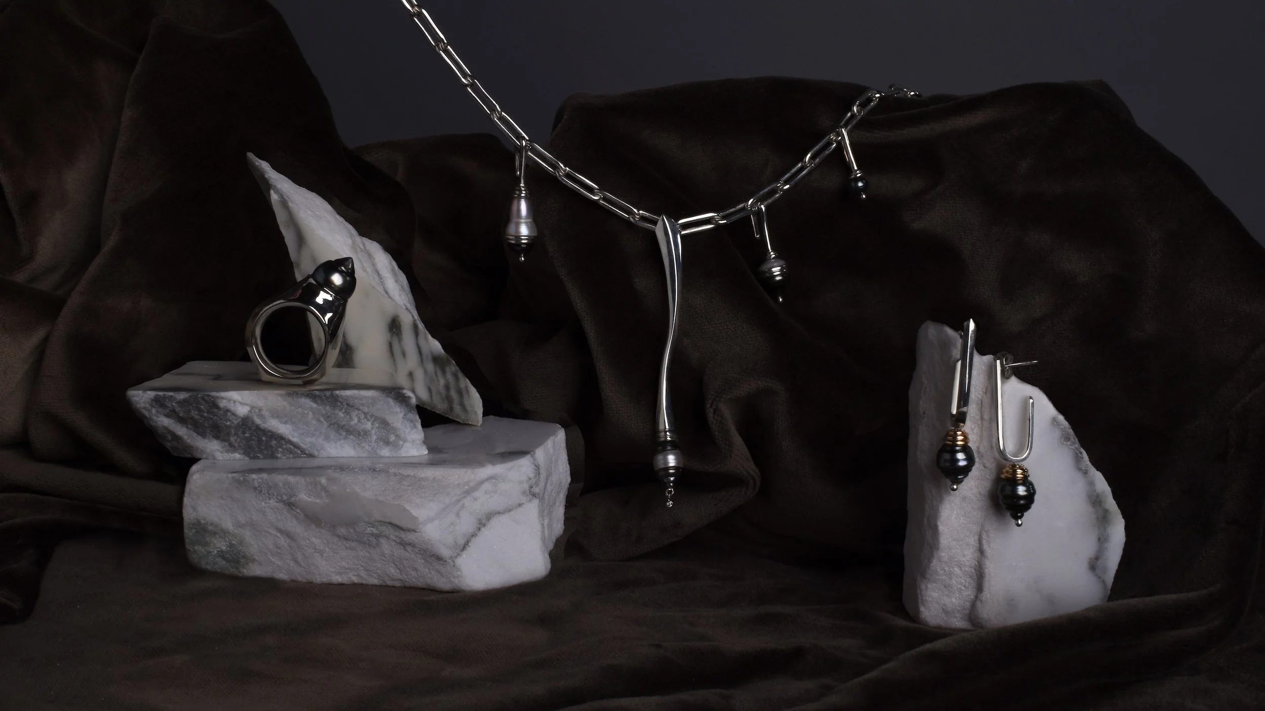 Still life image of statement pearl and silver ebb and flow collection, with Spindrift necklace, spinning Pearl Shore Ring, and Tahitian Pearl and gold Eddy earrings