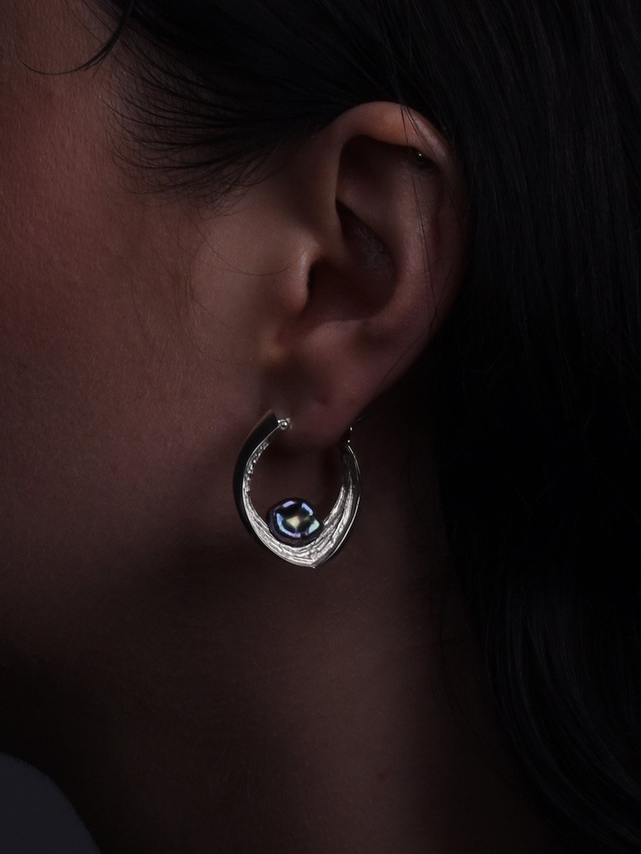 Close up of model wearing Cove hoop pearl earring, handmade from silver and peacock pearls.