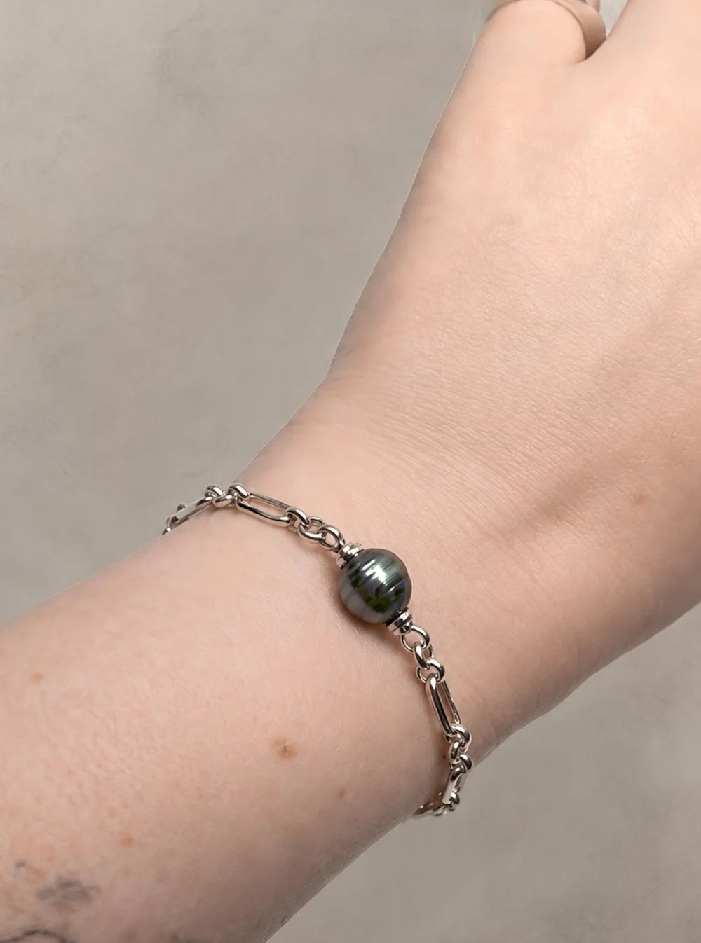 model wearing Eddy sterling silver Figaro chain bracelet by Charlotte Garnett, featuring a spinning Tahitian pearl with natural ridges.