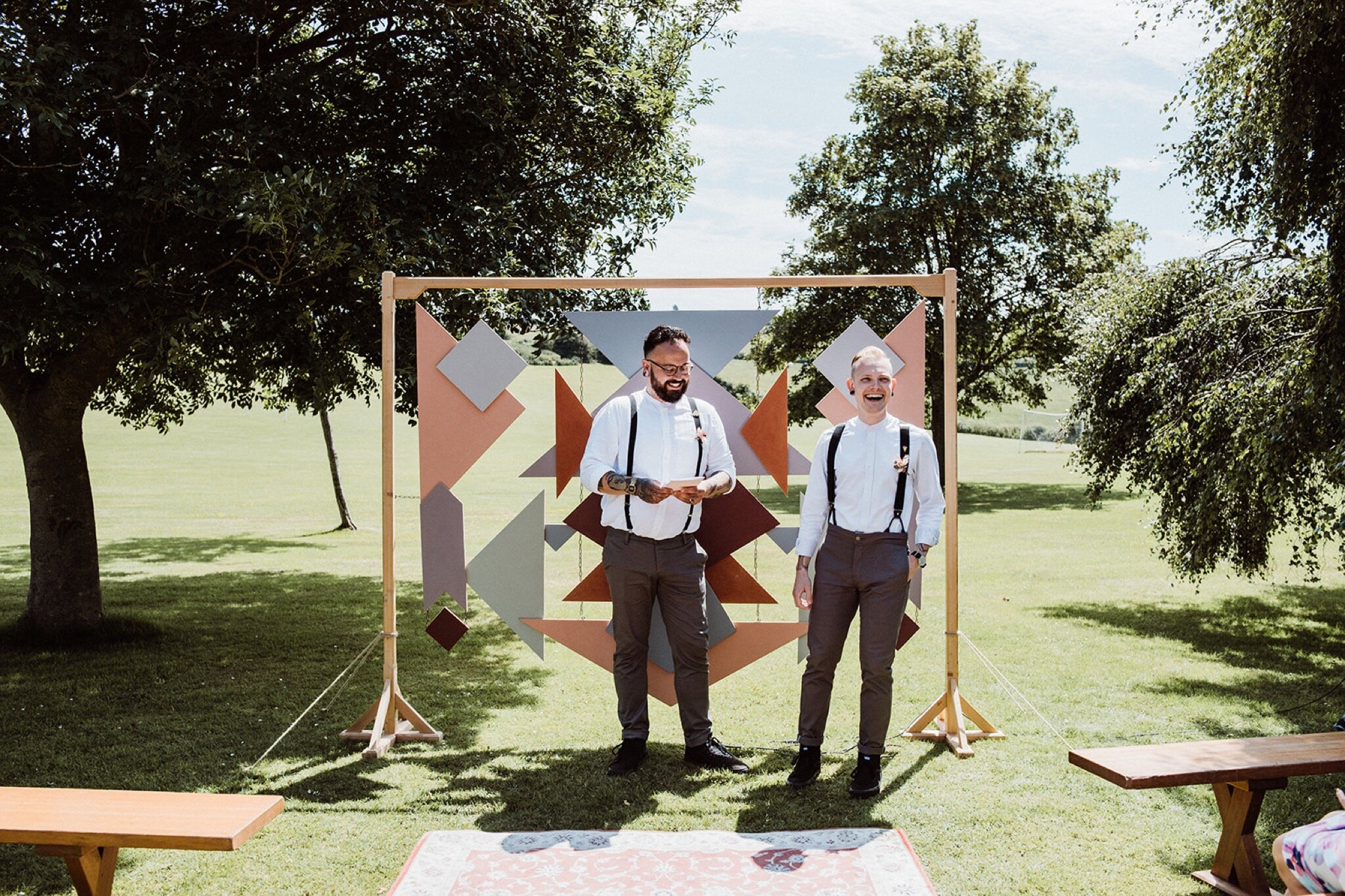 14_V+D Wedding-130_Groom and best man standing in front of a geometric wedding arch. Summer outdoor humanist wedding ceremony..jpg