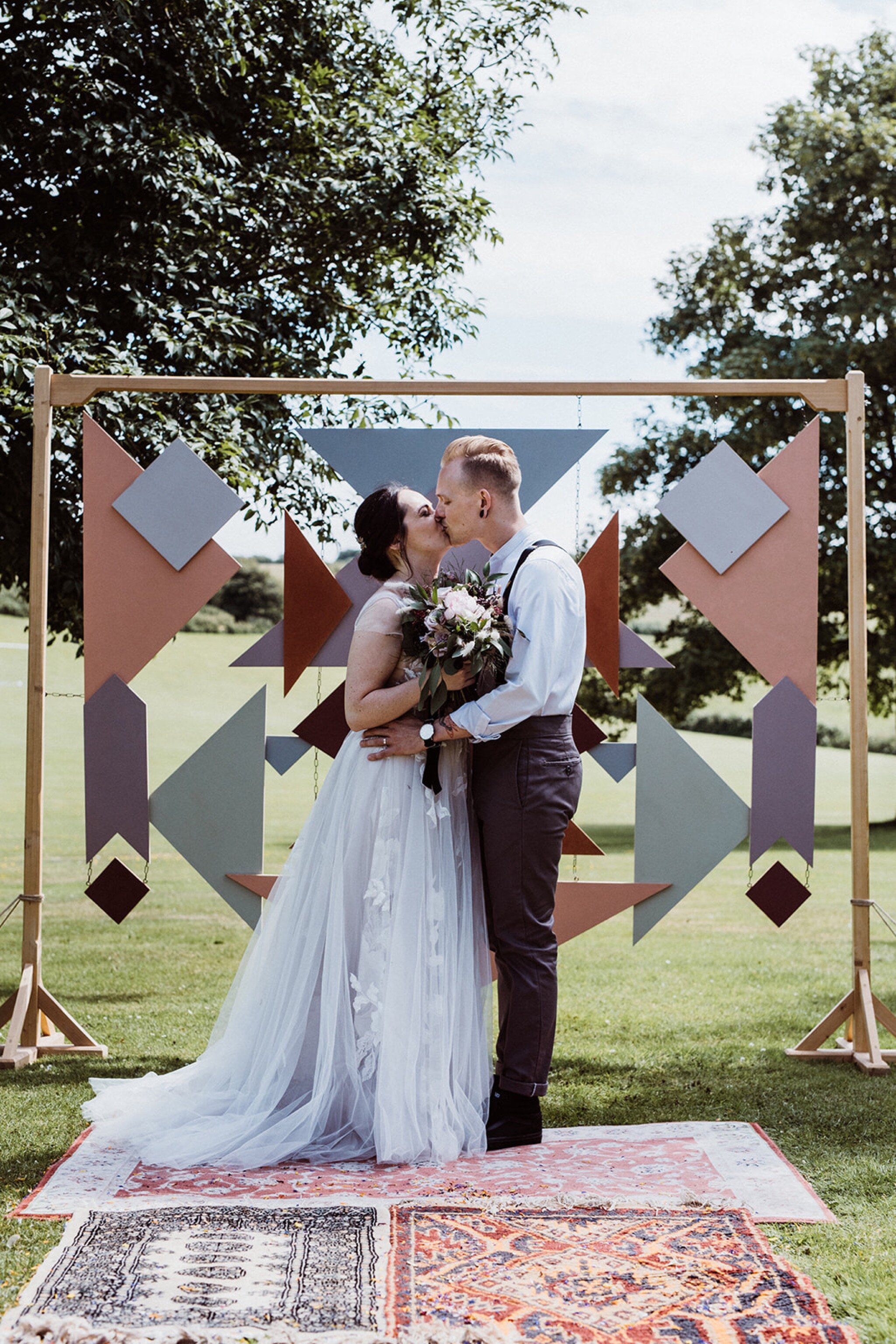 18_V+D Wedding-385_Bride and groom kissing in front of geometric wedding arch Summer outdoor humanist wedding ceremony..jpg