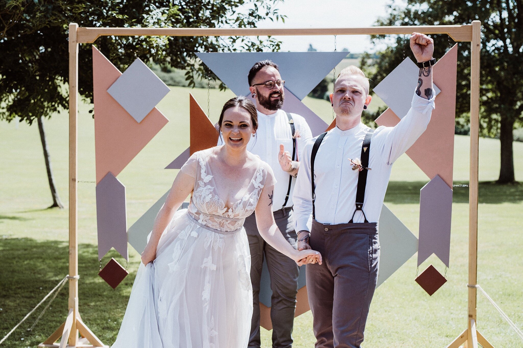 20_V+D Wedding-220_Groom putting his fist in the air in front of geometric wedding arch holding hands with bride..jpg