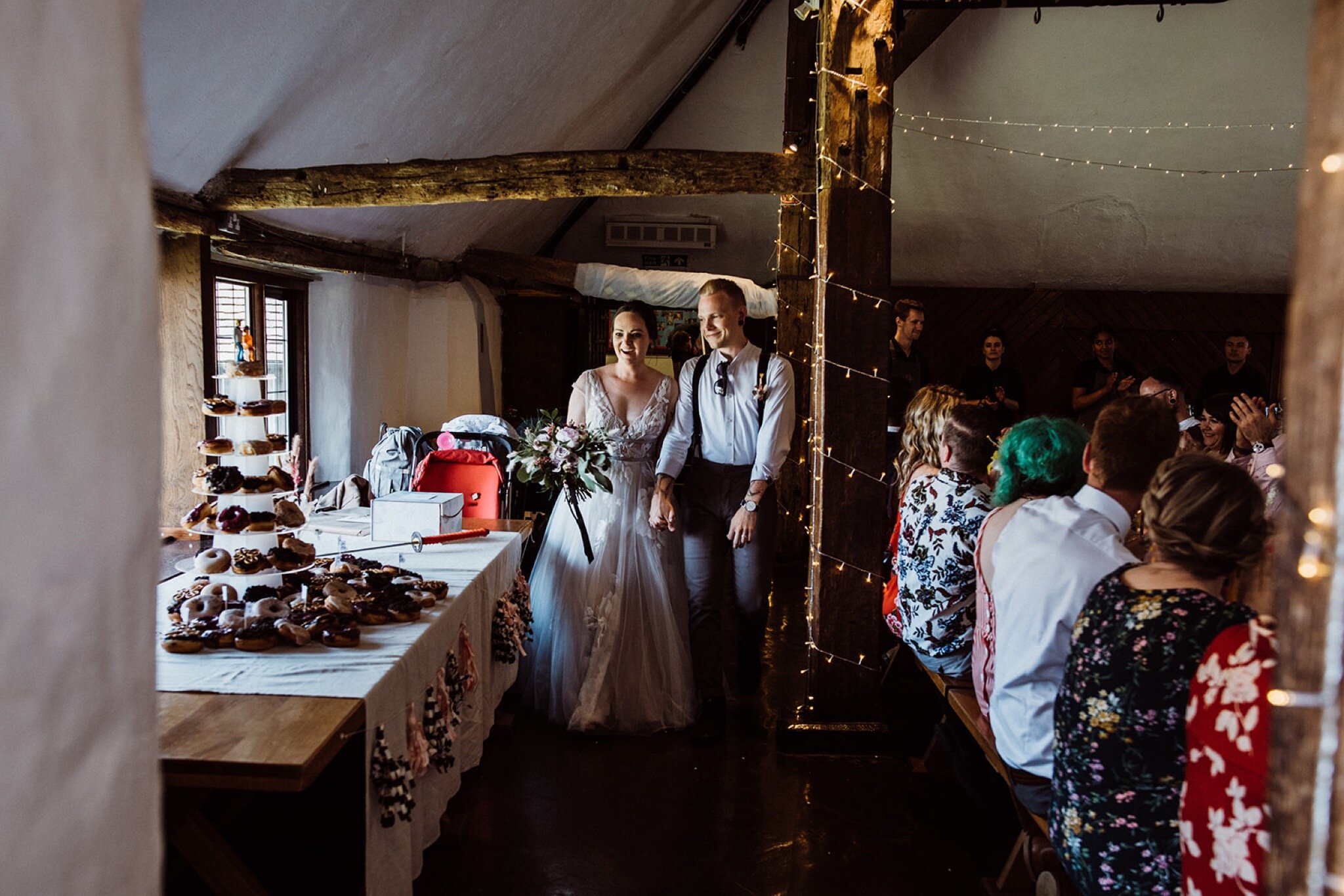 32_V+D Wedding-474_bride and groom lit from the left entering the wedding breakfast room and looking at the donut wedding cake%0A.jpg