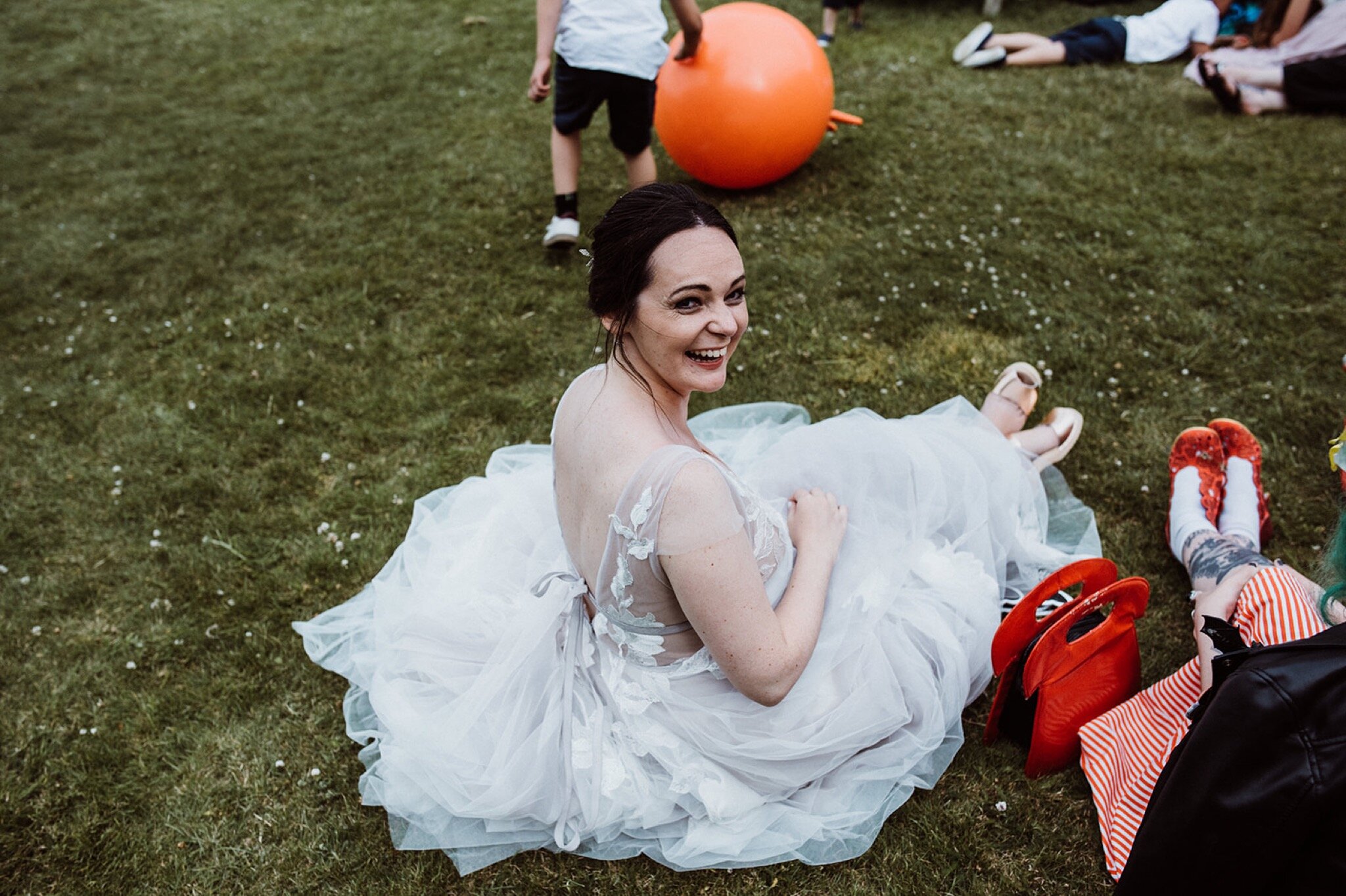 47_V+D Wedding-751_bride sat on grass laughing at the camera in tulle skirt%0A.jpg