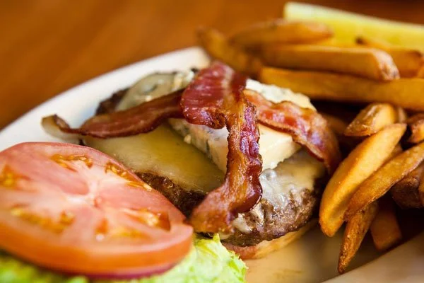 Close-up of a cheeseburger with bacon, tomato, lettuce, and French fries on the side.