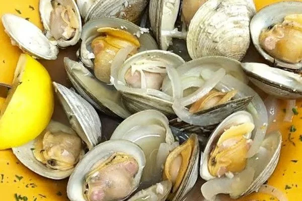 A yellow plate of steamed clams with chopped onions and herbs.
