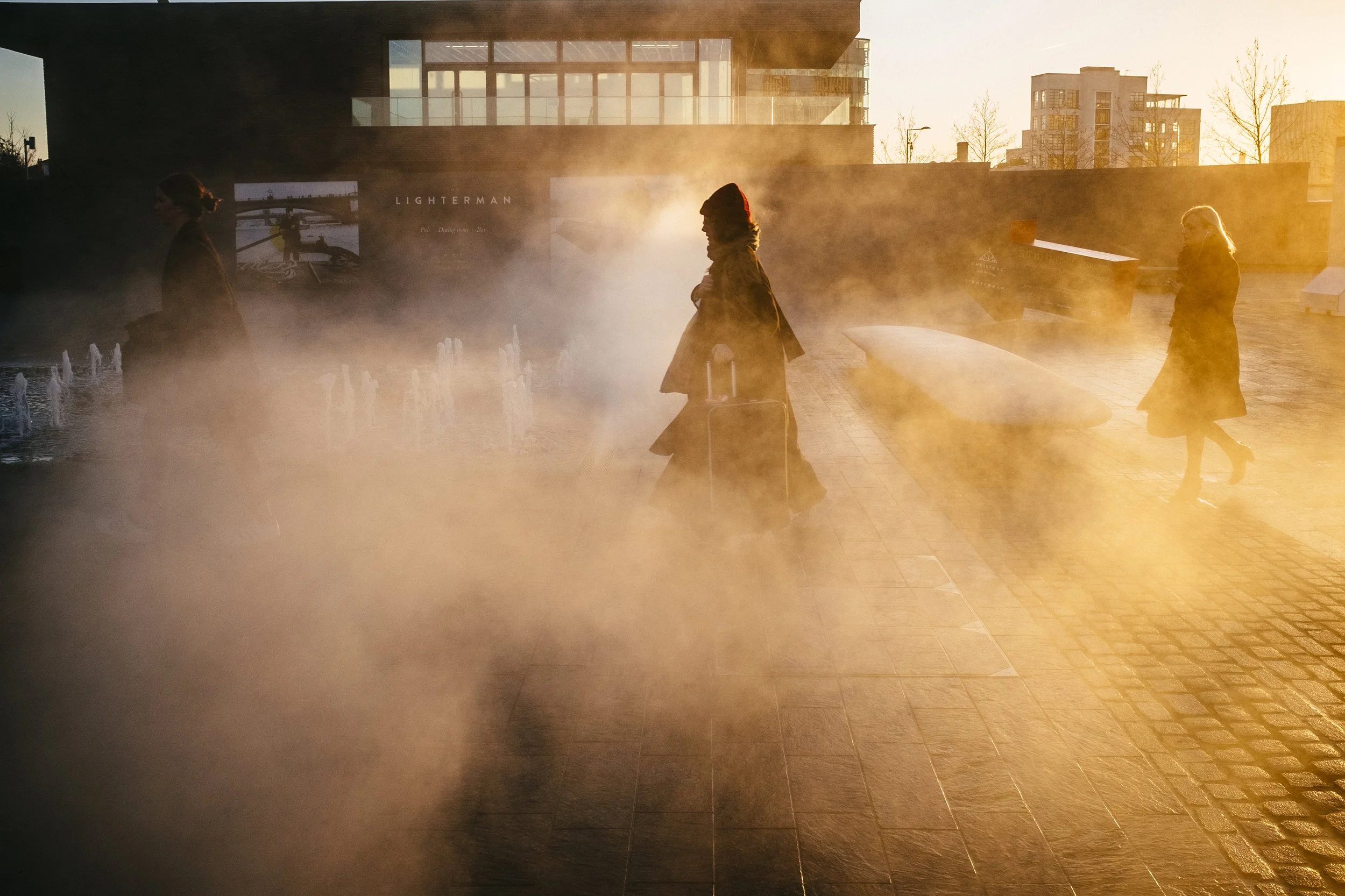Pedestrians walks through steam rising from a fountain on Granary Square, near King's Cross, London, Wednesday, Dec. 9, 2015.