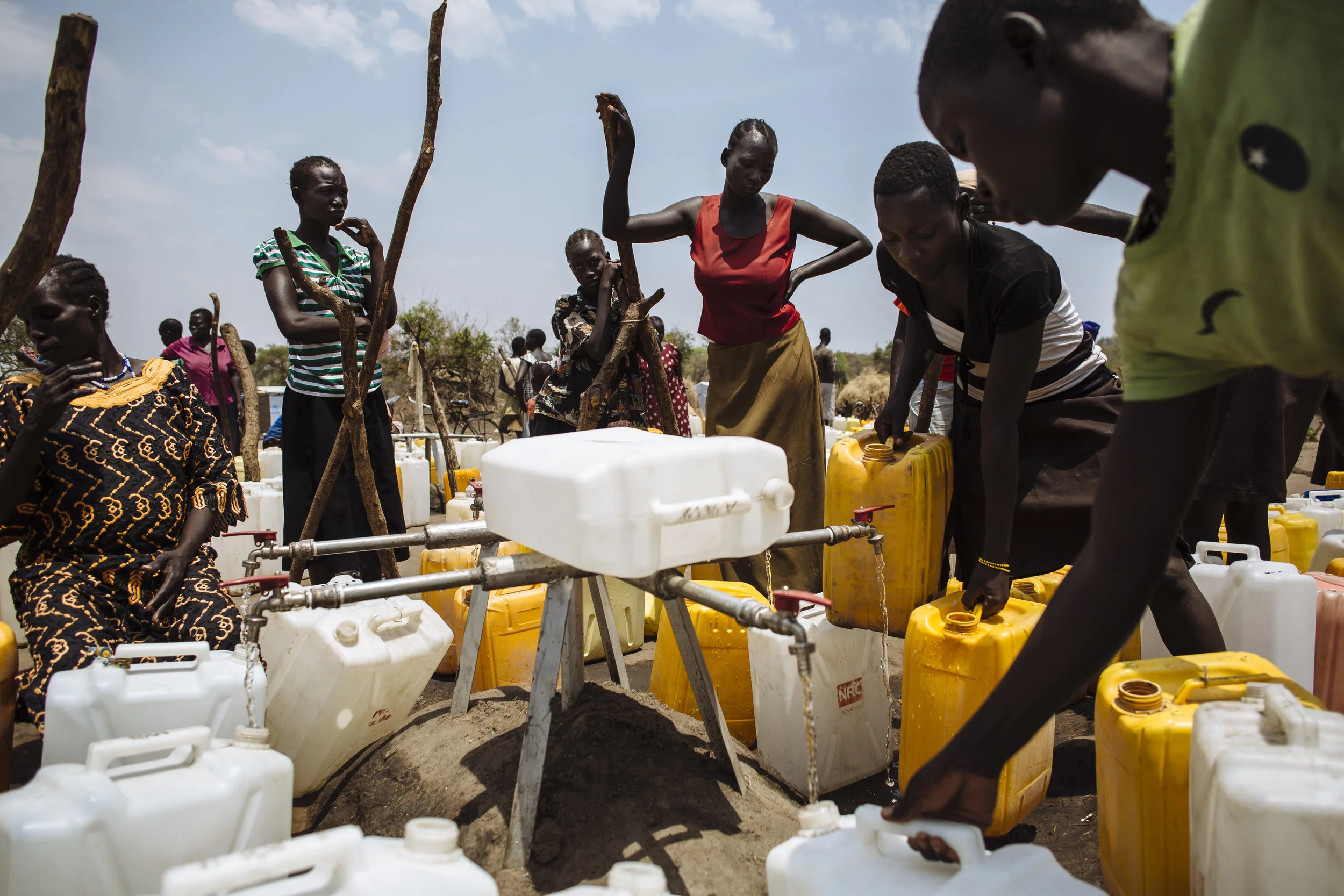 South Sudanese refugees fill jerry cans with water from a water point in Bidibidi refugee settlement, Yumbe District, Northern Region, Uganda. Fetching water often involves hours of waiting due to high demand, despite the tank being filled twice daily by a water truck.