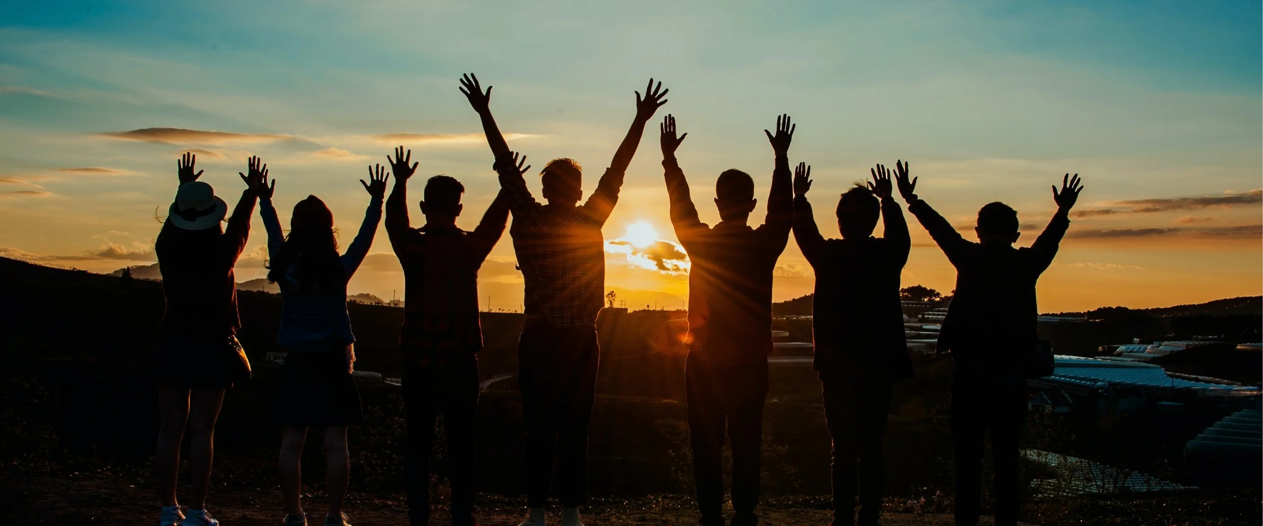People standing on top of a mountain at sunrise with their arms lifted