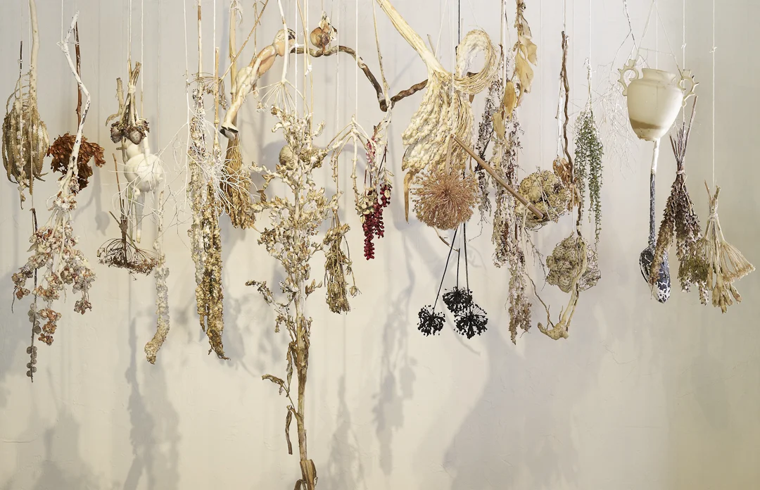 installation with high altitude plant material, vase, and doll, poircelain, wax and string