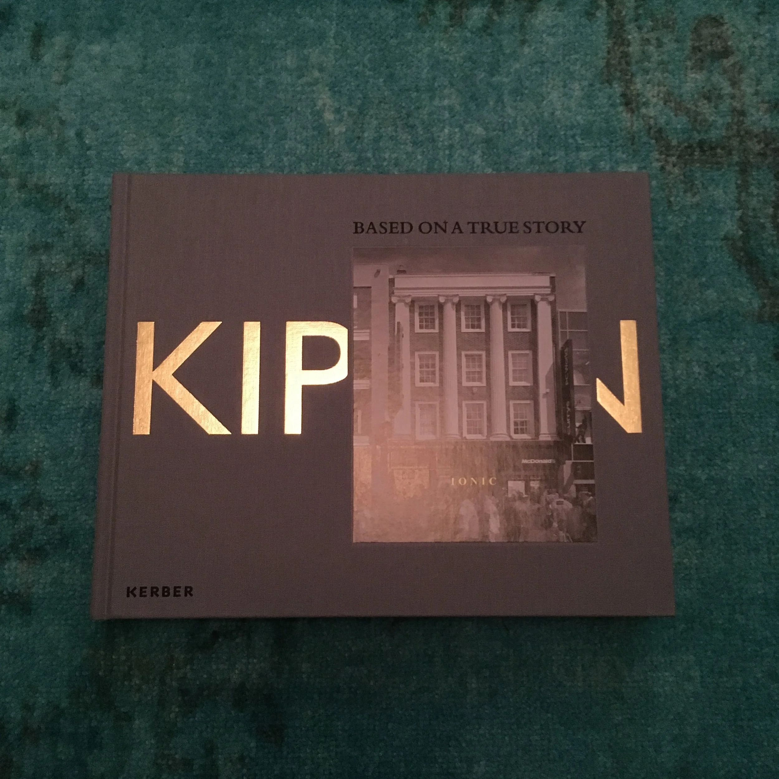  Image description: The front cover of a book with the name Kippin in large gold font, two letters of which are obscured behind a gloss image embedded into the surface of the cover that depicts a four story building with Grecian columns and sash wind