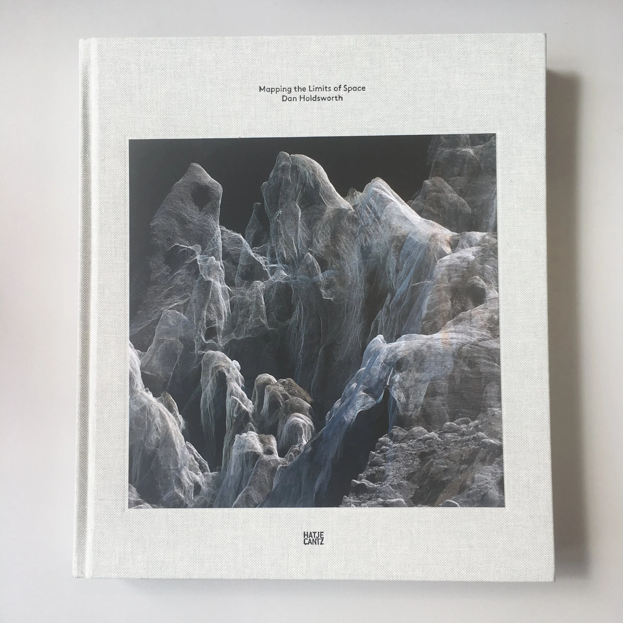  Image description: The front cover of a large book covered in off-white canvas, featuring an extremely finely rendered digital 3D point-cloud image of mountainous terrain in an array of white, grey and blue tones on a black background. The title emb