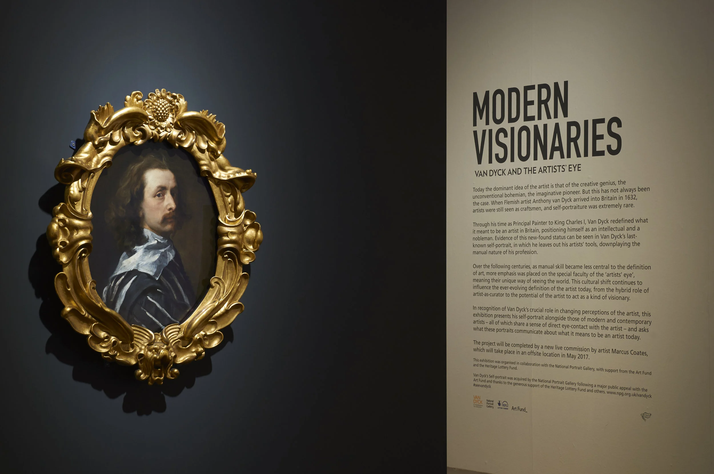  Image description: An install photo of the last-known self-portrait by Anthony Van Dyck, showing the artist with long wavy brown hair, wearing a blue and white striped blouse, and turning his head over his right shoulder to look out at the viewer. T