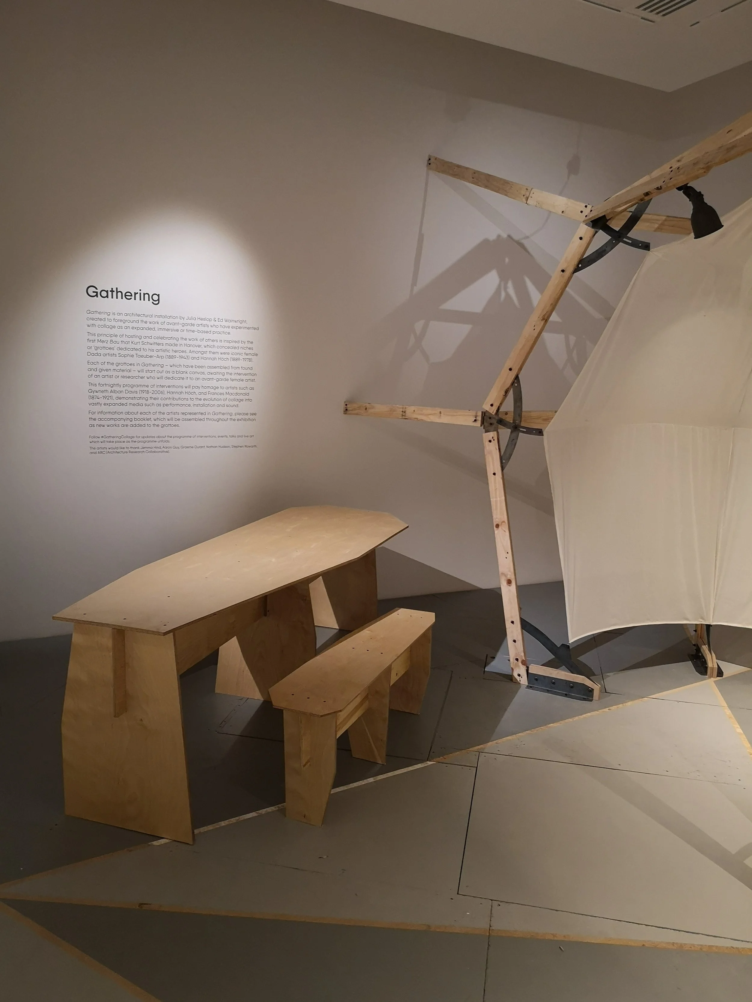  Image description: An installation photograph of the architectural commission 'Gathering', showing a corner of the gallery in which a cave-like structure made out of elegant wooden struts and stretched canvas is waiting to accommodate new artist com