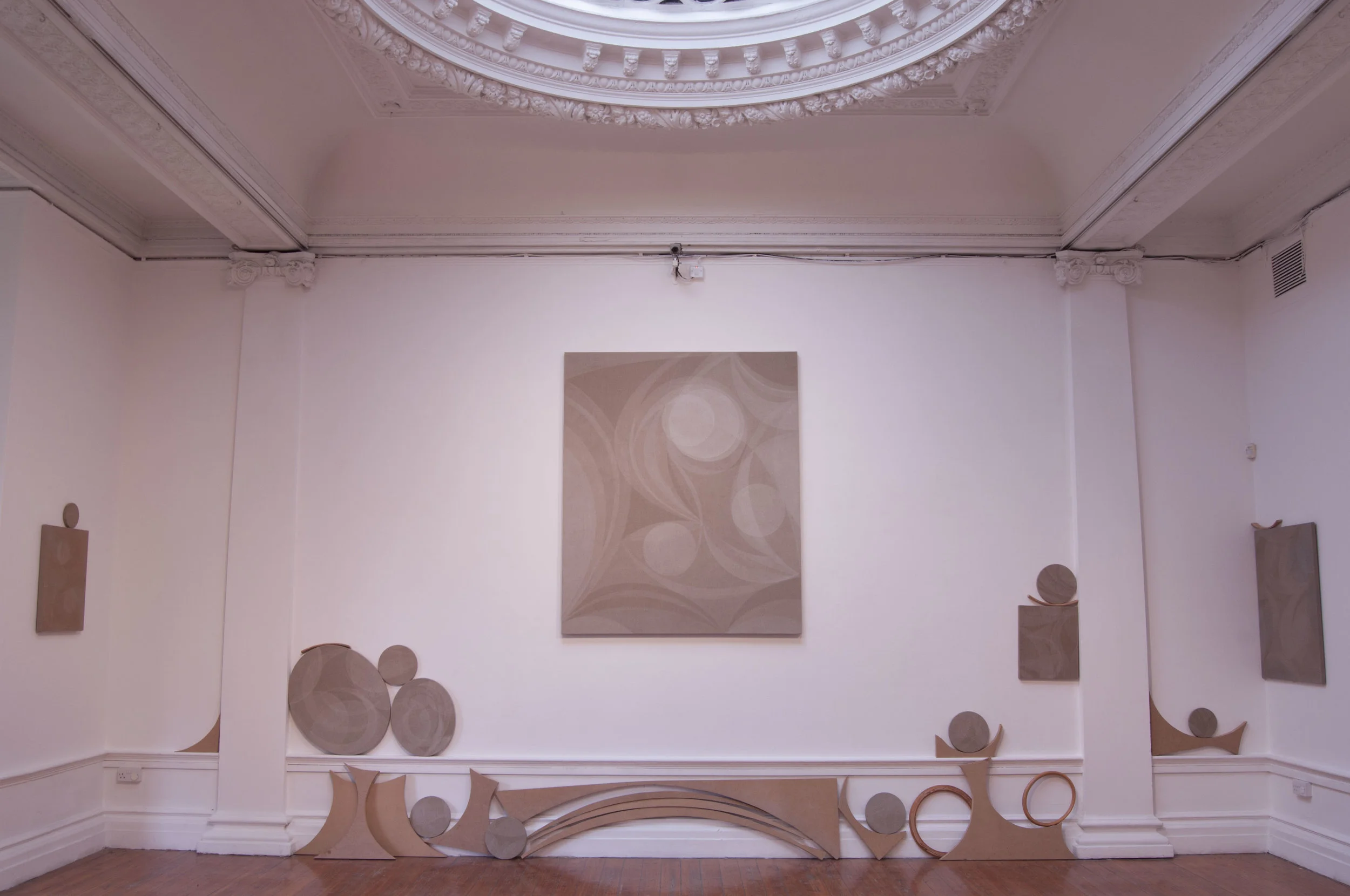  Image description: A series of paintings of different shapes and sizes play across the surface of a wall: all unframed and sharing the same visual palette of iridescently pale curves and circles. Beneath the largest central canvas in the middle of t