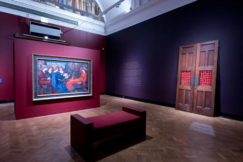  Image description: An install photo of the final room of ‘The Enchanted Interior’ exhibition, in a grand gallery with a vaulted ceiling and rich purple walls, on which can be seen two artworks: on the left, ‘Laus Veneris’ by the Pre-Raphaelite paint