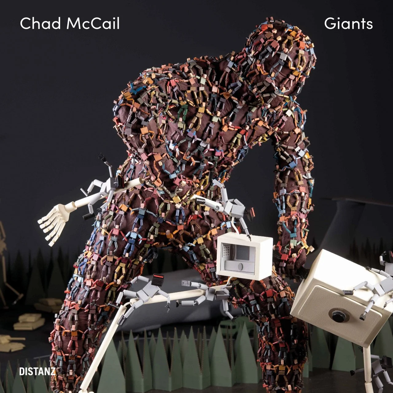  Image description: A square book cover showing a human-like sculpture comprised of hundreds of small figures made of multi-coloured blocks that appear to have their arms interlocked. The large human-like figure is slightly bent forward, holding the 