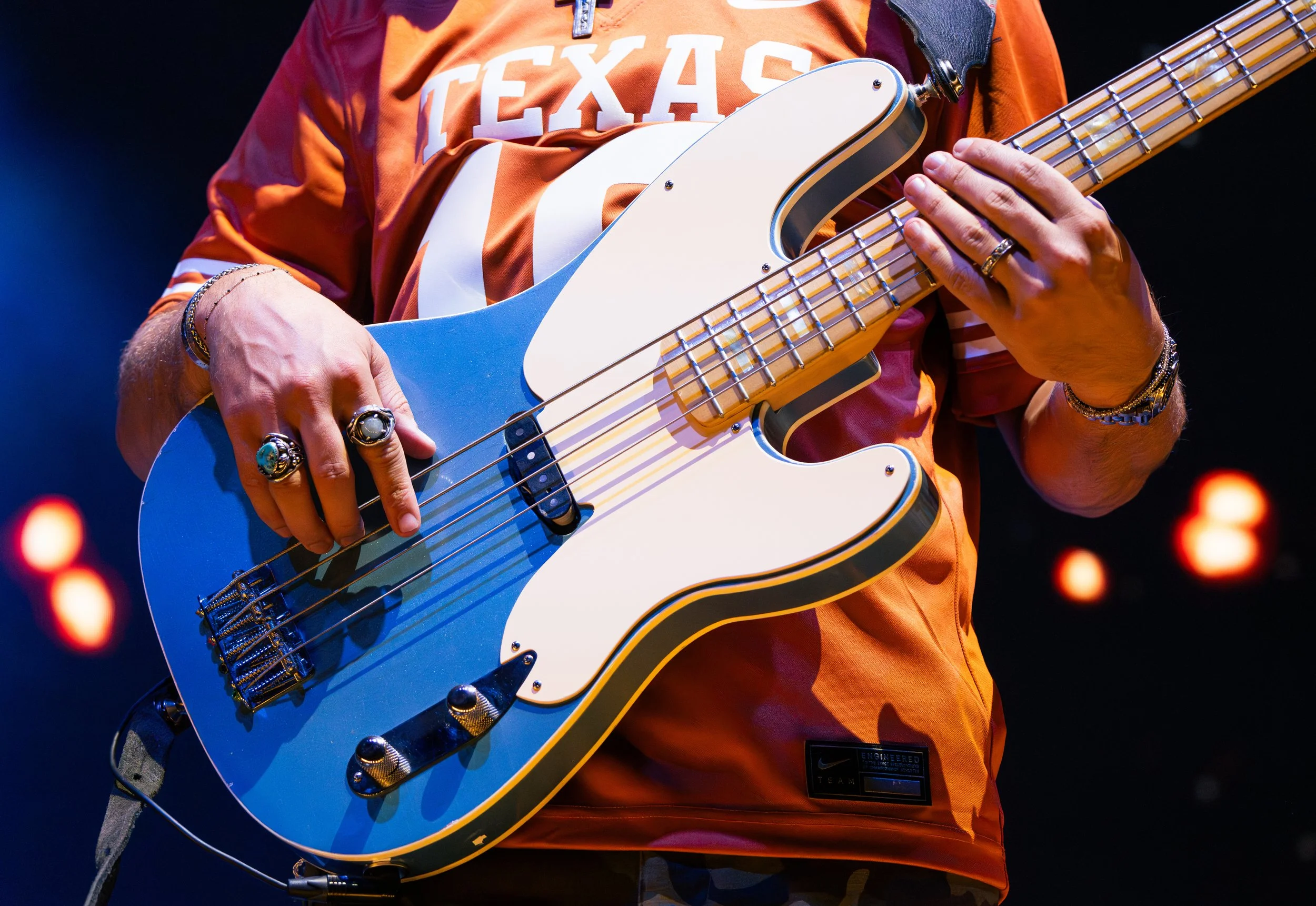 Bass player Andrew Bishop dons a University of Texas jersey and bright blue guitar while playing melodic guitar riffs.