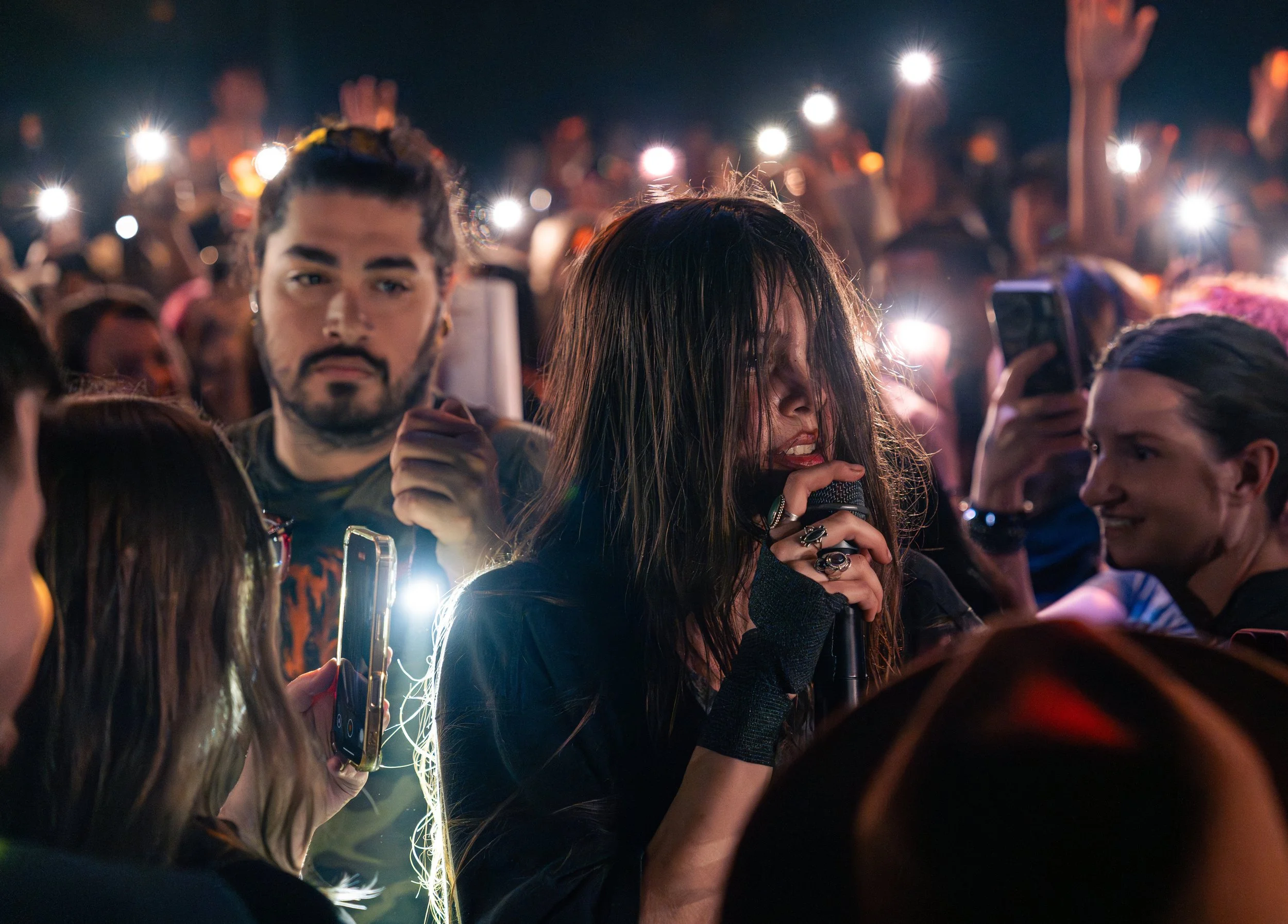  Isella walks through the crowd singing the hushed yet profound lyrics of “All of Human Knowledge Made Us Dumb”: “Turns out, all of human knowledge at our fingertips made us dumb / Lost my connection to reality stepping into a virtual one.” 