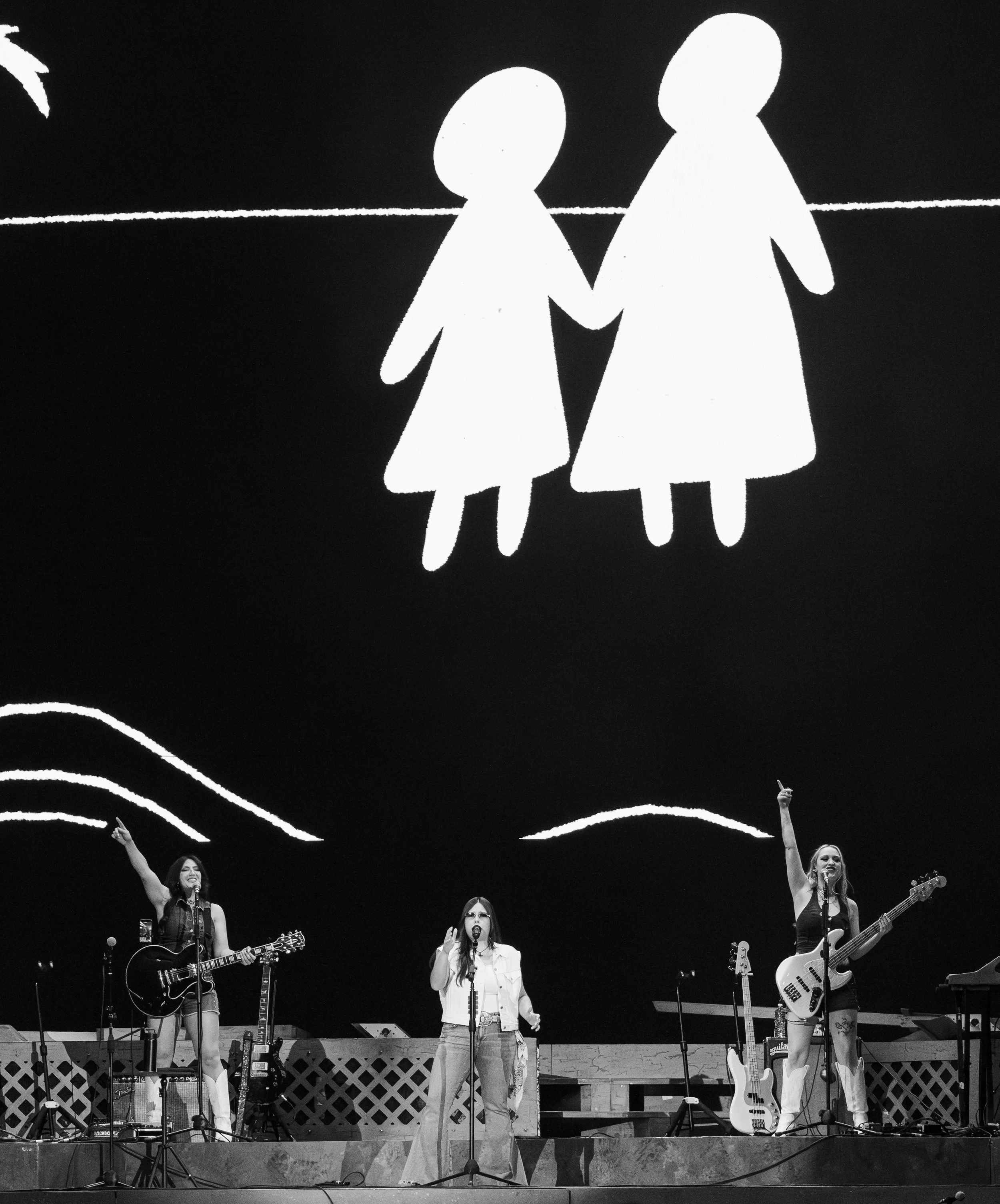  Gigi Perez and guitarists Aubrey Harris and Sonya Rae Taylor hold up their hands to the sky while singing “At the Beach, in Every Life”: “Is sayin’ if my dreams come up empty / And I wash up on the shore / You would find me at the beach / In every l