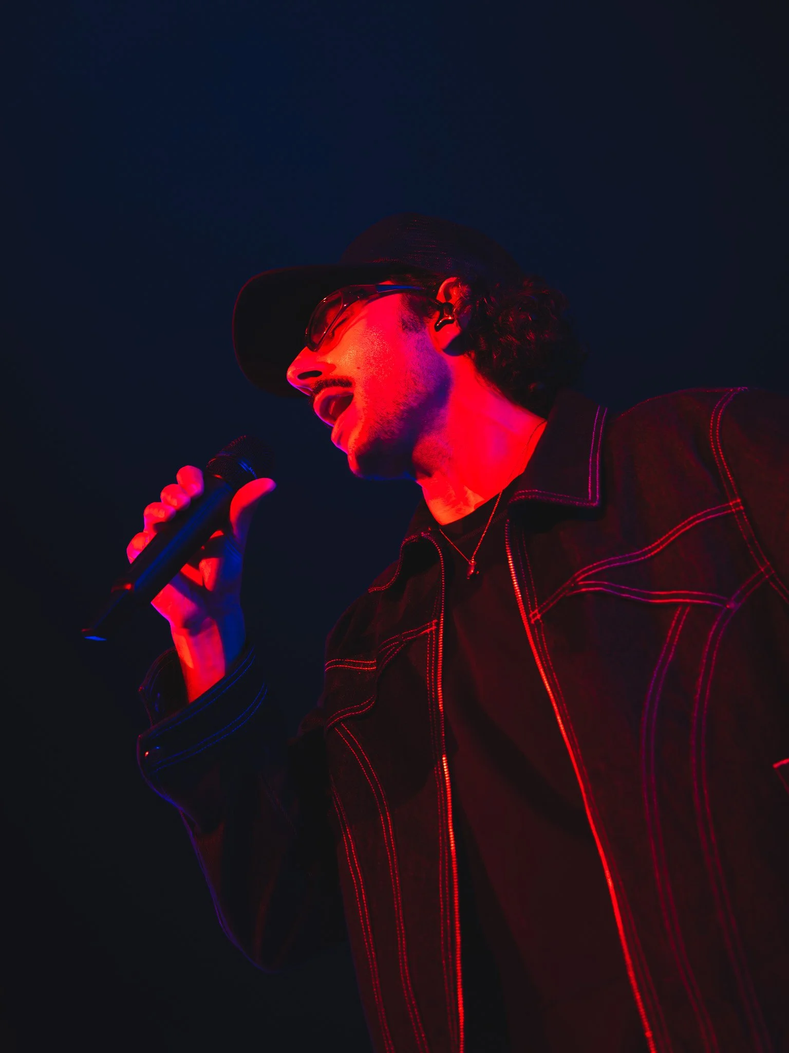  Vocalist Majid Al Maskati sings into the microphone under red stage lights during his performance of “Cold.” 