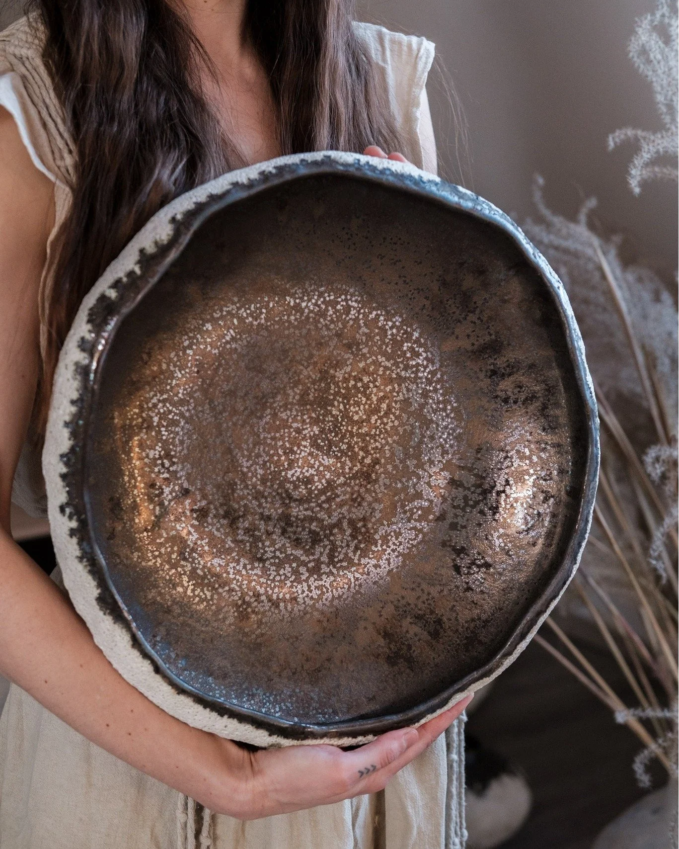 This large centrepiece bowl brings together elemental contrast &mdash; at its centre, a luminous bronze glaze gathers like liquid light, while along the rim, a raw lava inlay reveals cratered texture reminiscent of the moon&rsquo;s surface.

Each ima