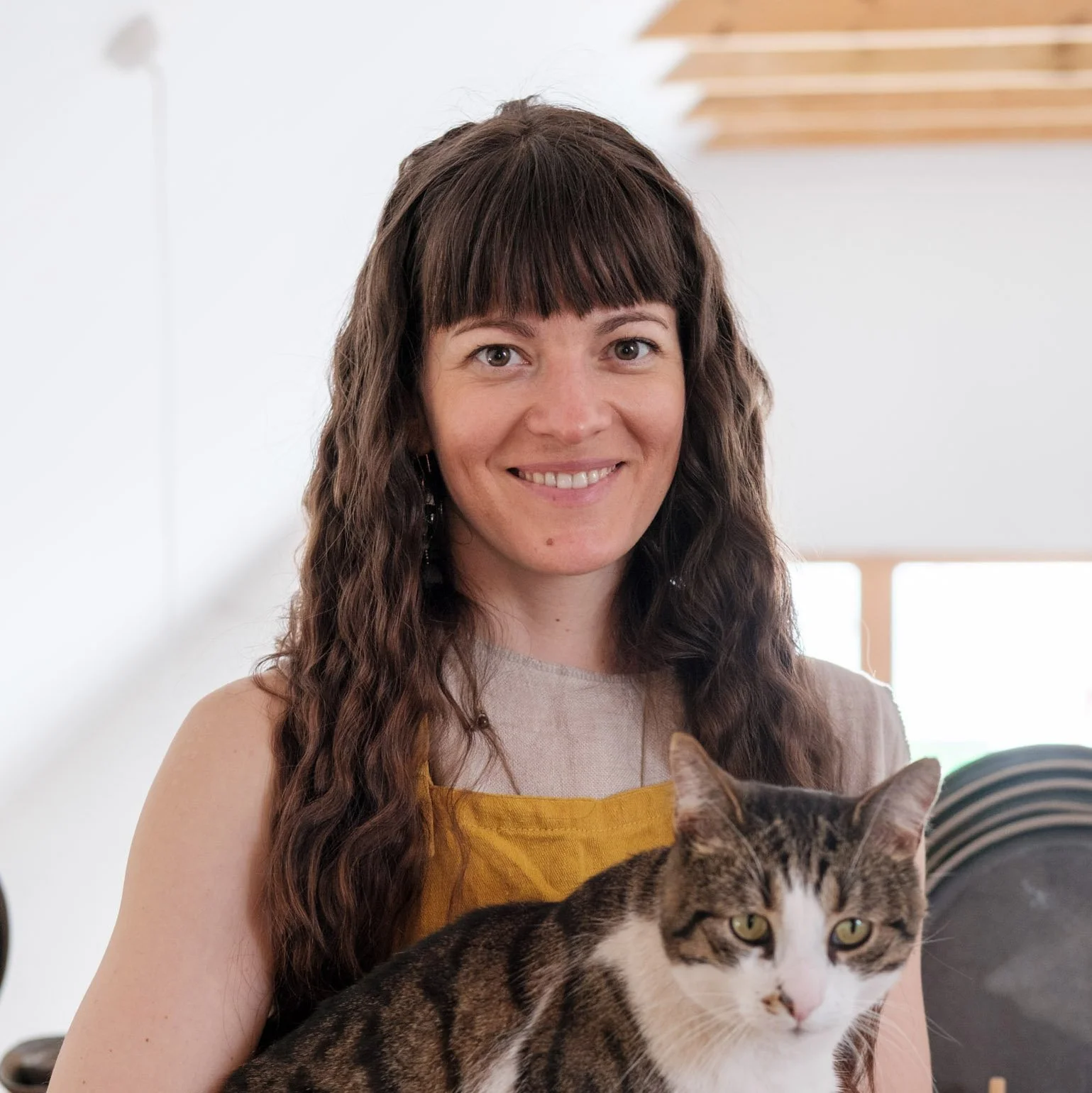 A woman holding two cats inside a cozy, modern home with wooden beams and decor.