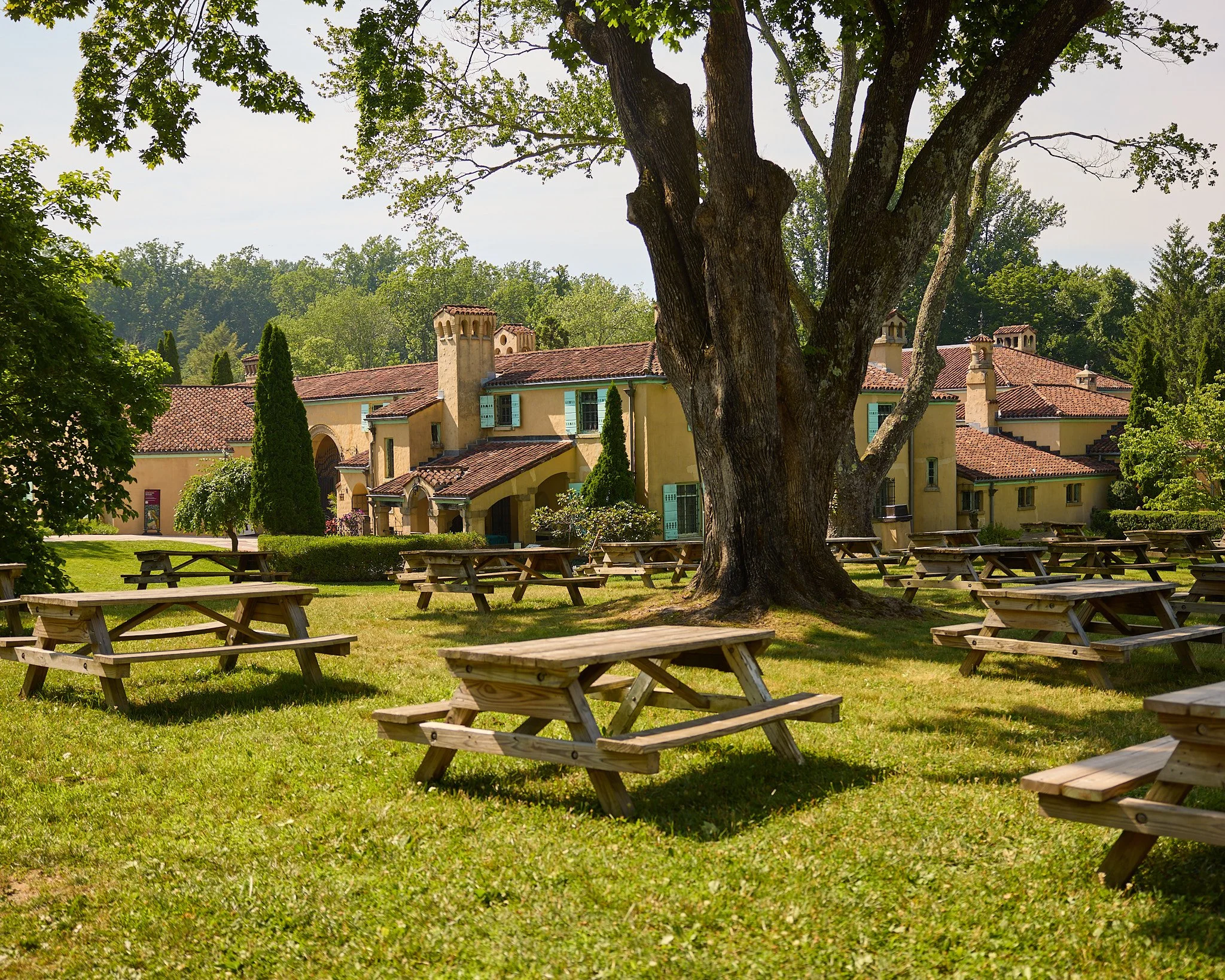 The Italianate Rosen House at Caramoor in Katonah, NY, framed by a large shade tree with empty picnic tables on the lawn in front.