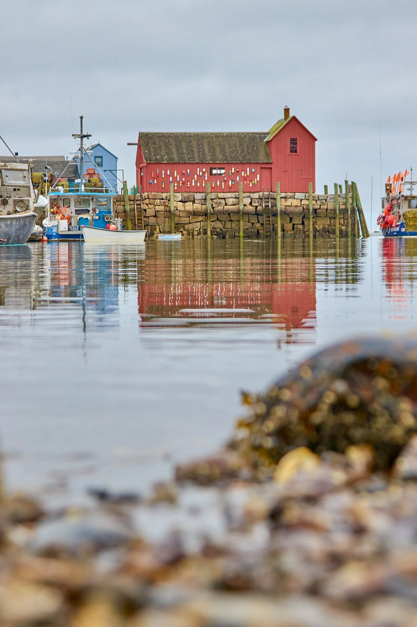 Motif No. 1 red fishing shack reflected in Rockport harbor with blurred rocky shoreline in the foreground