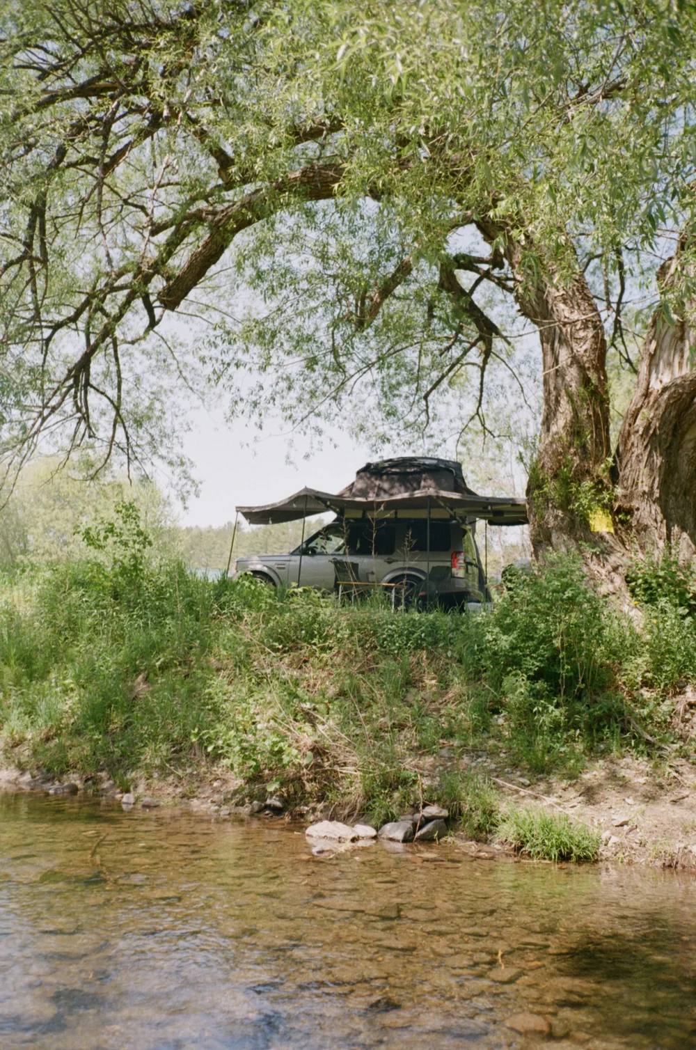 Land Rover L4 with rooftop tent under tree by river
